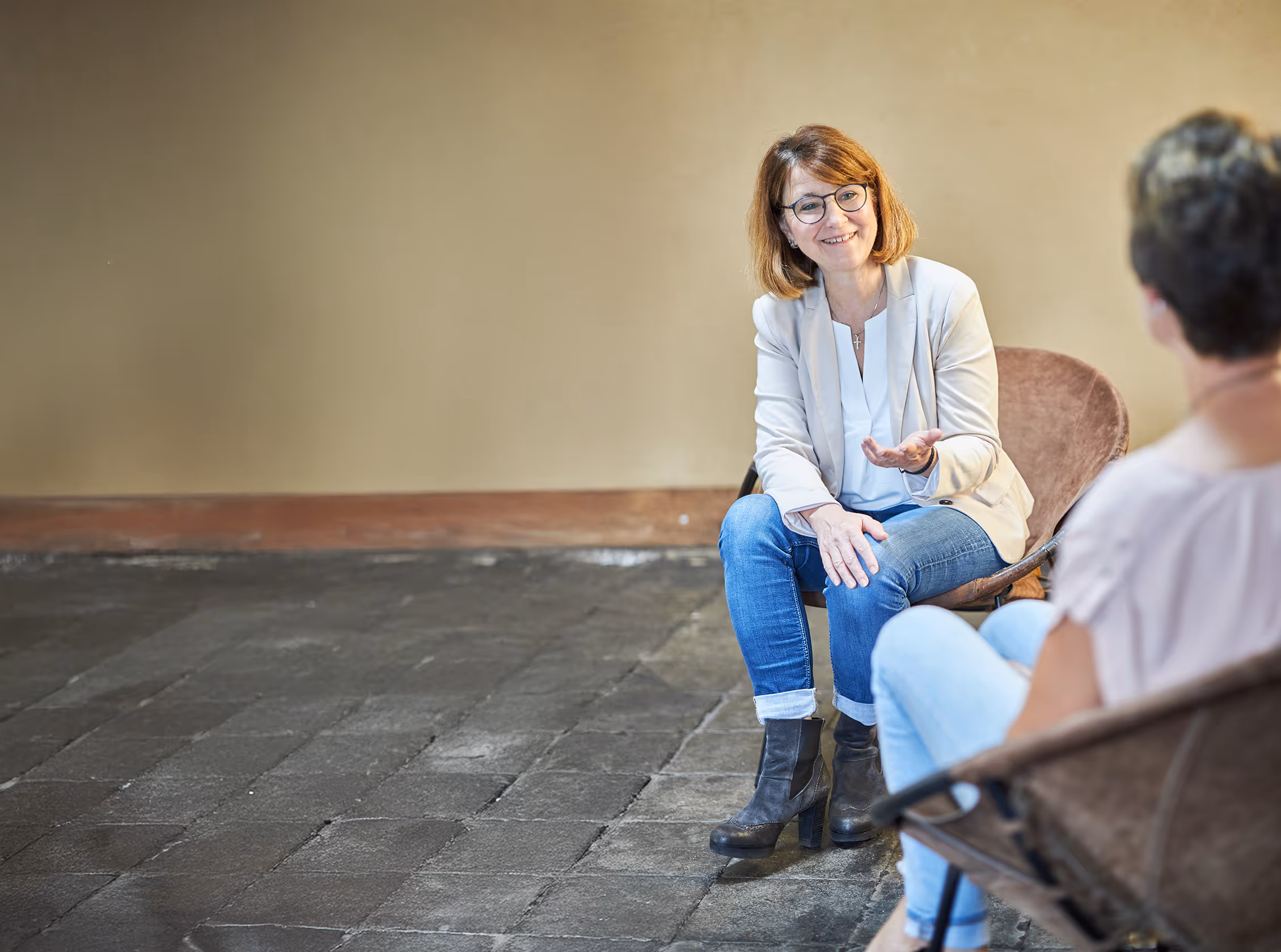 Zwei Frauen im Gespräch in einem schlichten Raum mit Steinboden – Coaching- oder Beratungssituation mit offener Gestik und persönlicher Atmosphäre