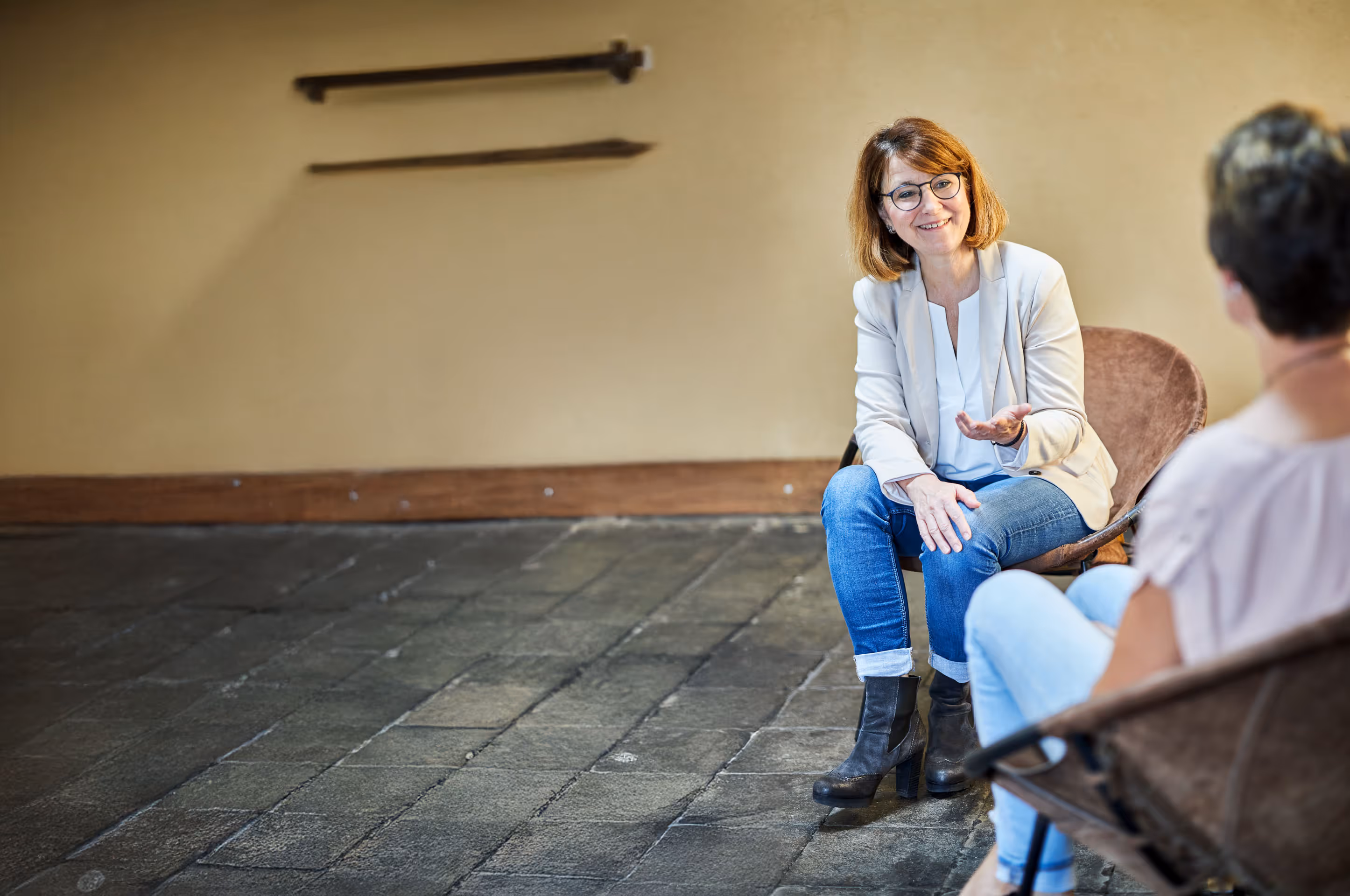Zwei Frauen im Gespräch in einem schlichten Raum mit Steinboden – Coaching- oder Beratungssituation mit offener Gestik und persönlicher Atmosphäre
