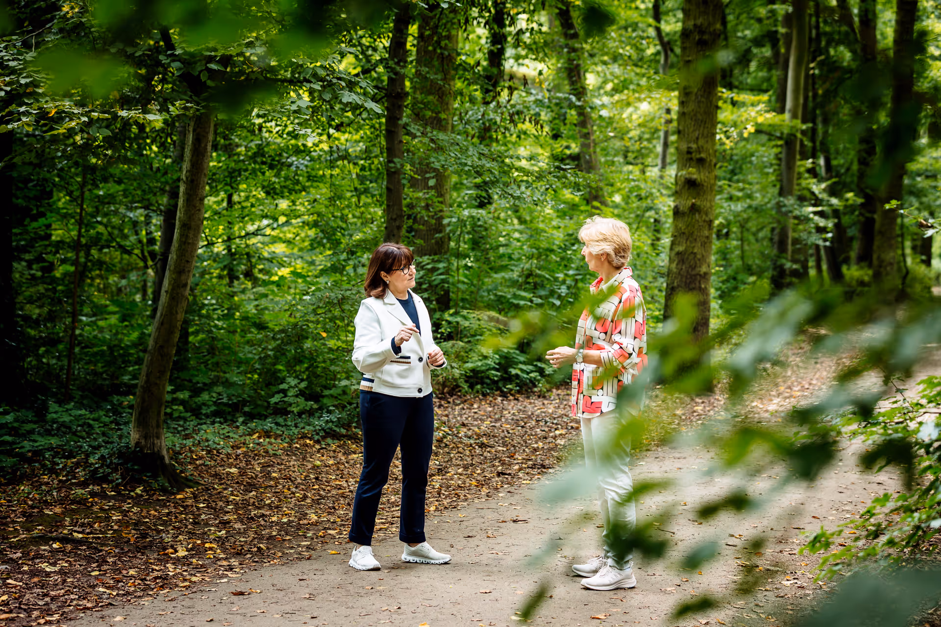 Zwei Frauen im Gespräch auf einem Waldweg – naturverbundene Beratung oder Coaching in entspannter Atmosphäre