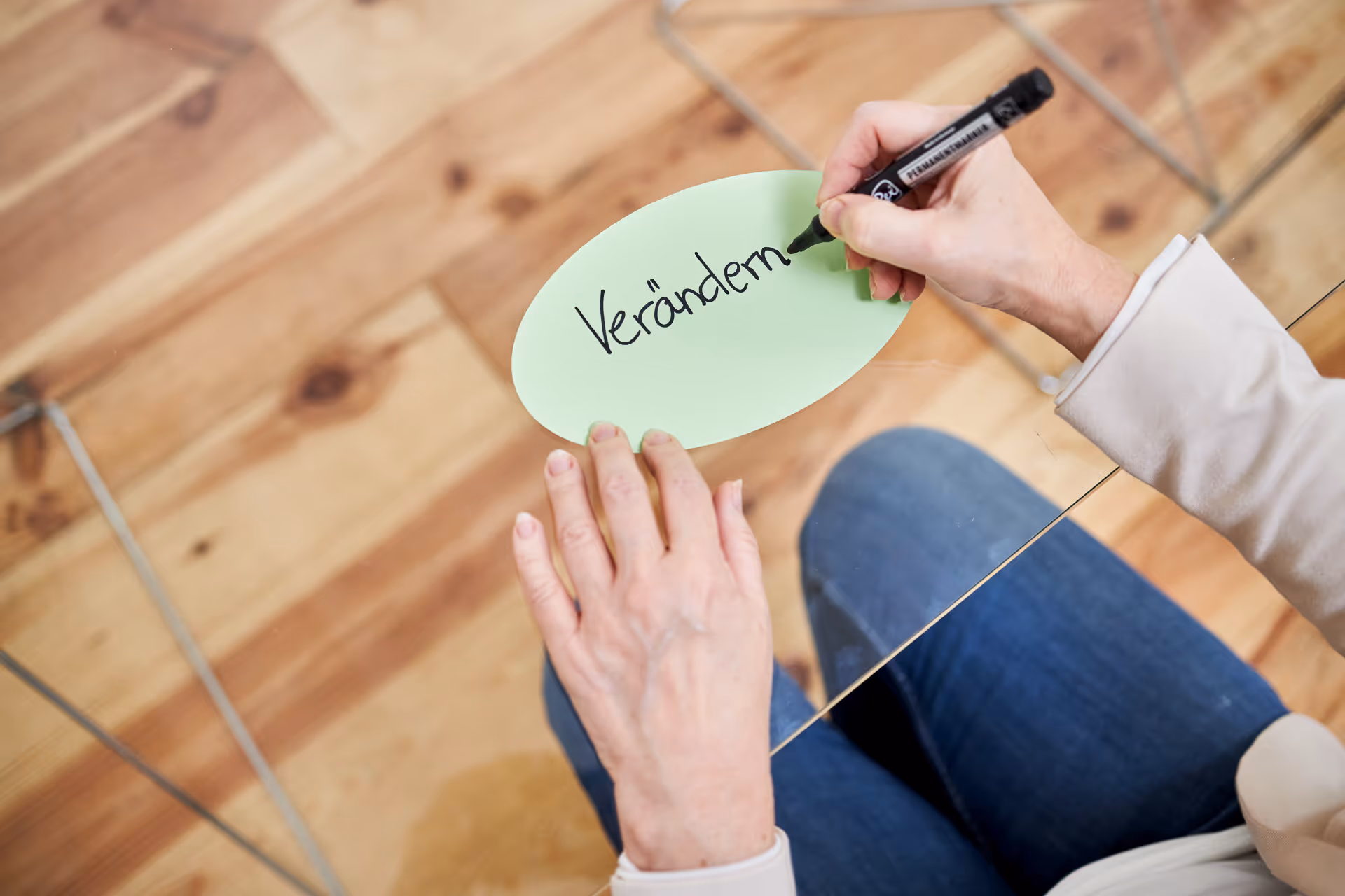 Frau schreibt mit einem Marker das Wort ‚Verändern‘ auf eine grüne Moderationskarte – Symbolbild für Wandel und Entwicklung