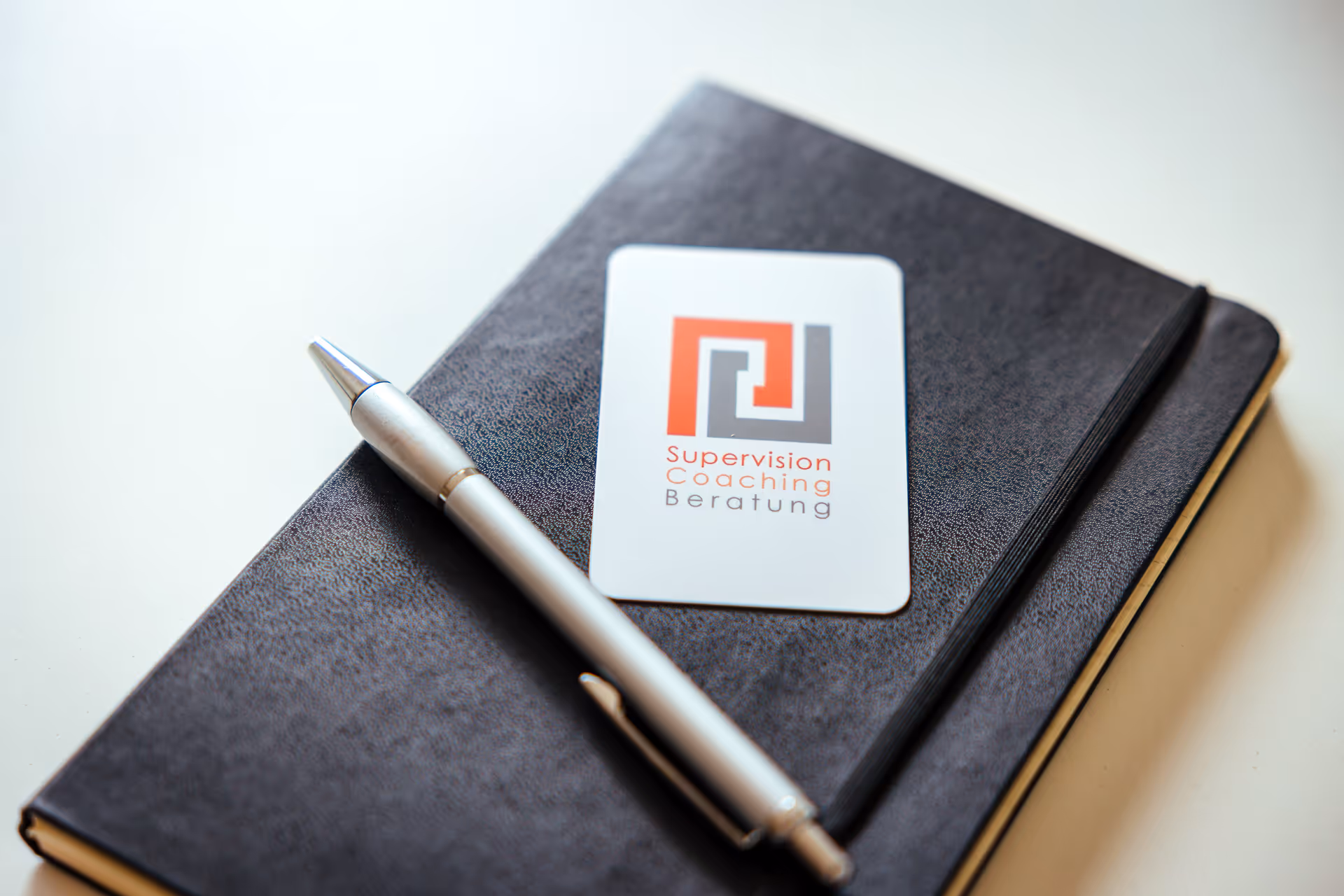 Notizbuch mit Kugelschreiber und Visitenkarte – Aufschrift: Supervision, Coaching, Beratung.