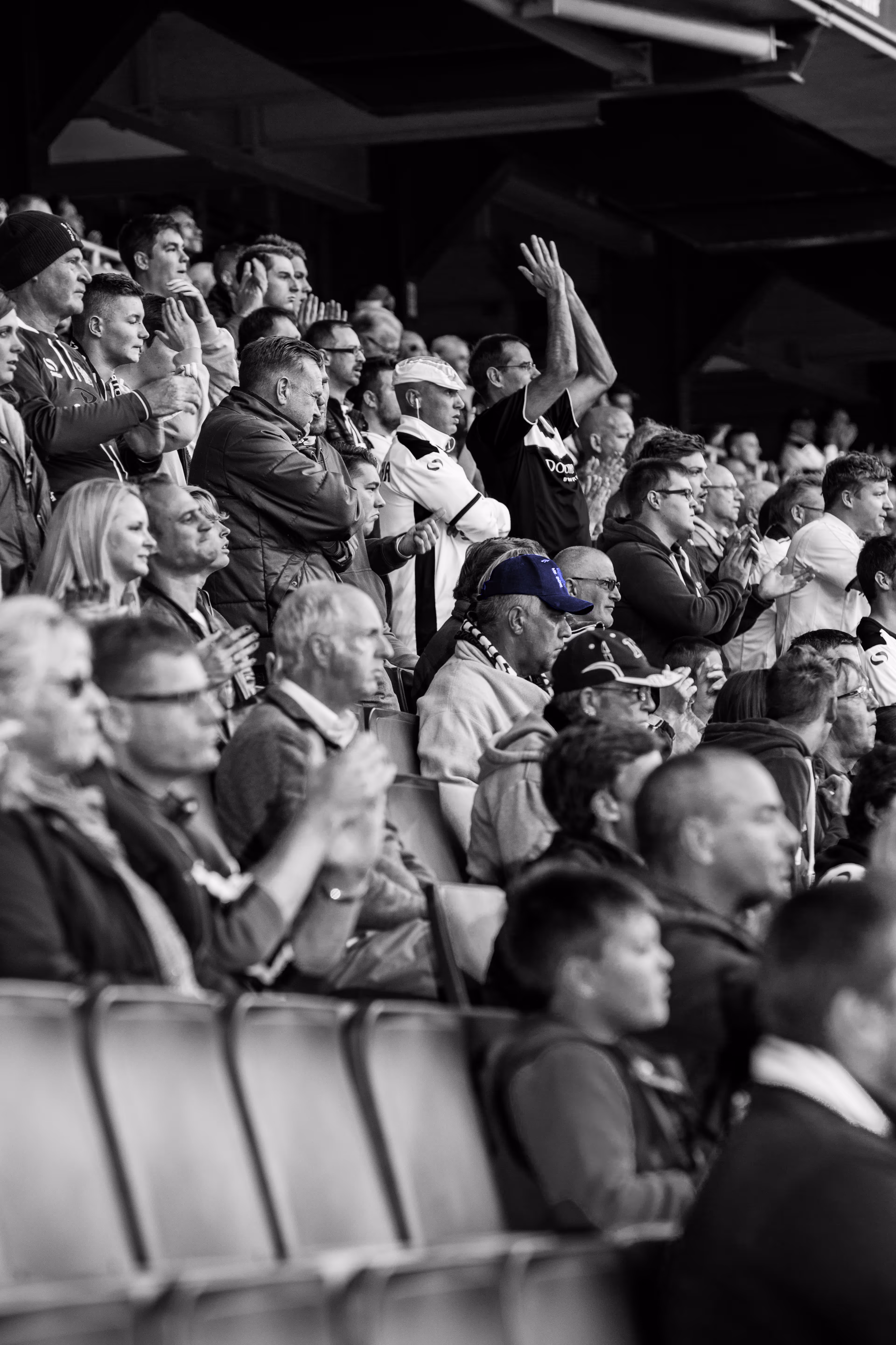 Aficionados apasionados por su equipo de futbol, en blanco y negro, un hombre porta una gorra lila