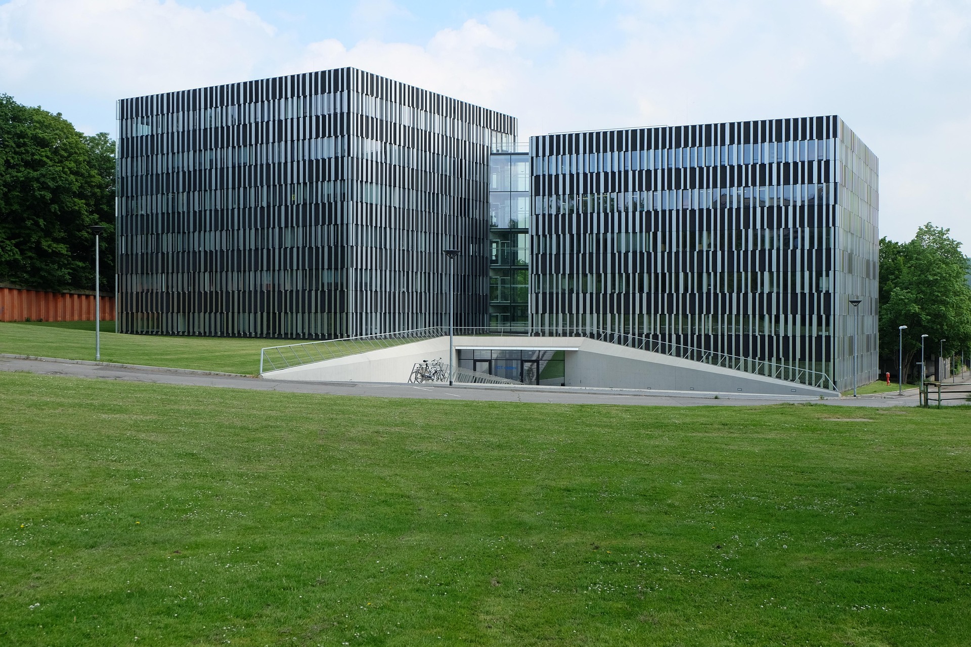Außenansicht des modernen RWTH Aachen Campus mit Glasfassade und großzügiger Grünfläche im Vordergrund.