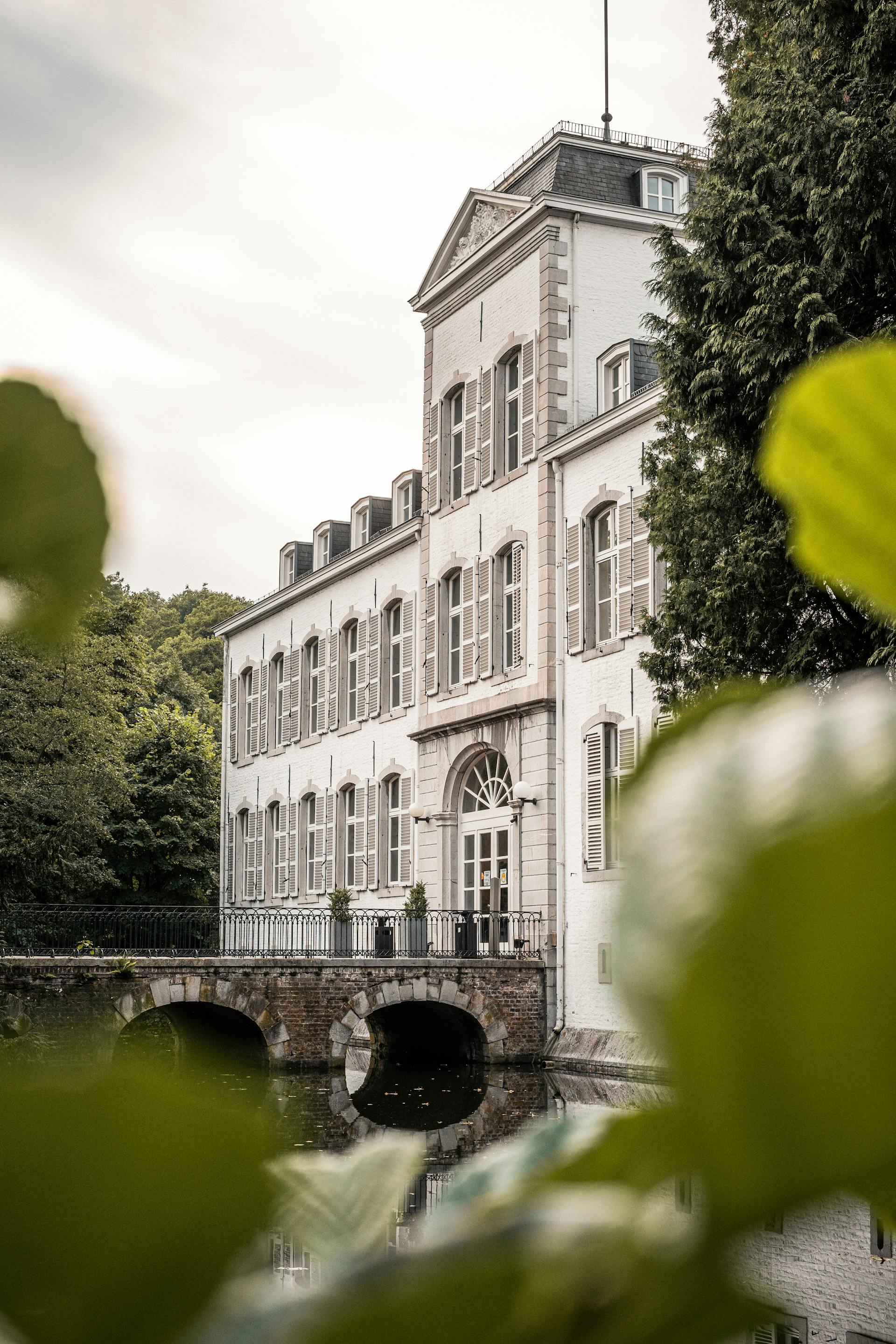 Historisches Gebäude mit Wassergraben in einem grünen Stadtviertel von Aachen, umgeben von Bäumen und Natur.