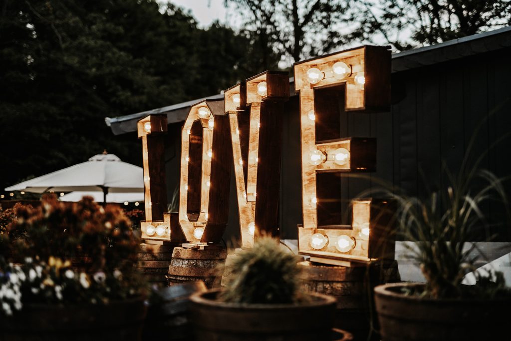 Große beleuchtete Buchstaben, die das Wort LOVE auf einem Außenbereich mit Pflanzen und Bäumen bilden.