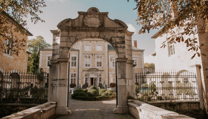 Steinerner Bogen mit Blick auf einen gepflegten Garten und ein historisches Gebäude im Hintergrund.