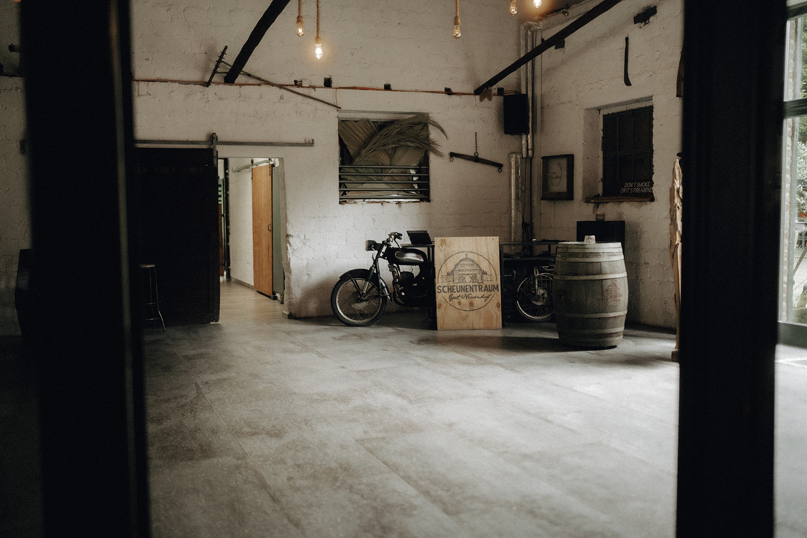 Helle Scheune mit weißem Backstein, einem Motorrad, Weinfass und einem Schild mit der Aufschrift ‚Scheunentraum‘.