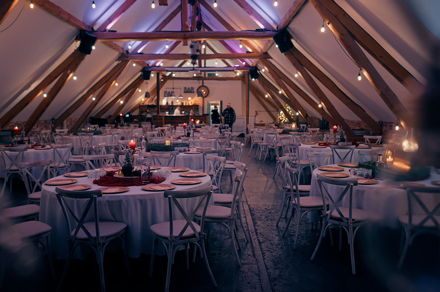 Rustikal dekorierter Veranstaltungsraum im Dachgeschoss mit runden, gedeckten Tischen und warmen Lichterketten.