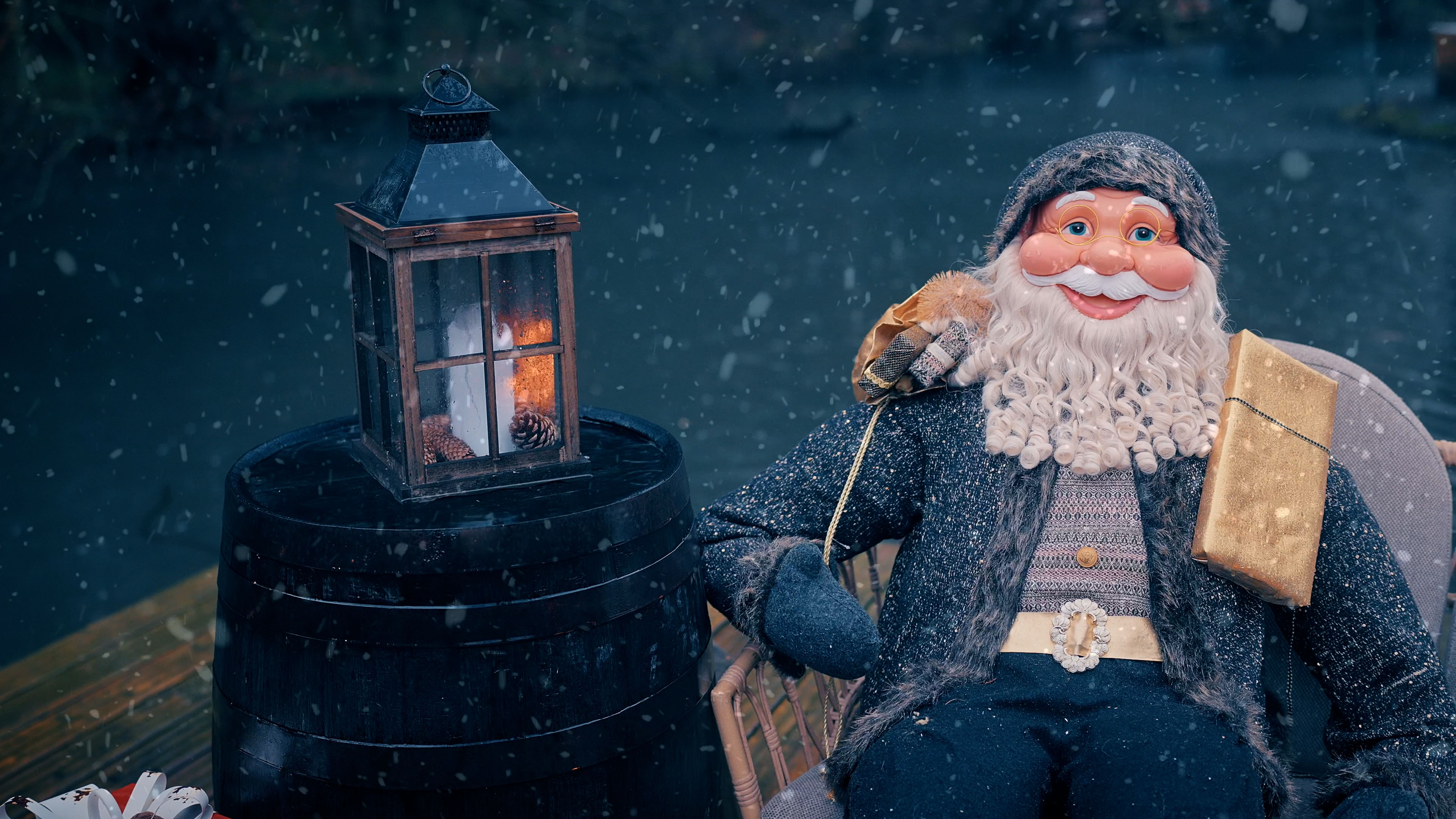 Weihnachtsmann-Dekoration mit weißem lockigem Bart, Brille, grauer Mütze, Sitz auf Stuhl neben einem Fass mit Laterne und Schnee.