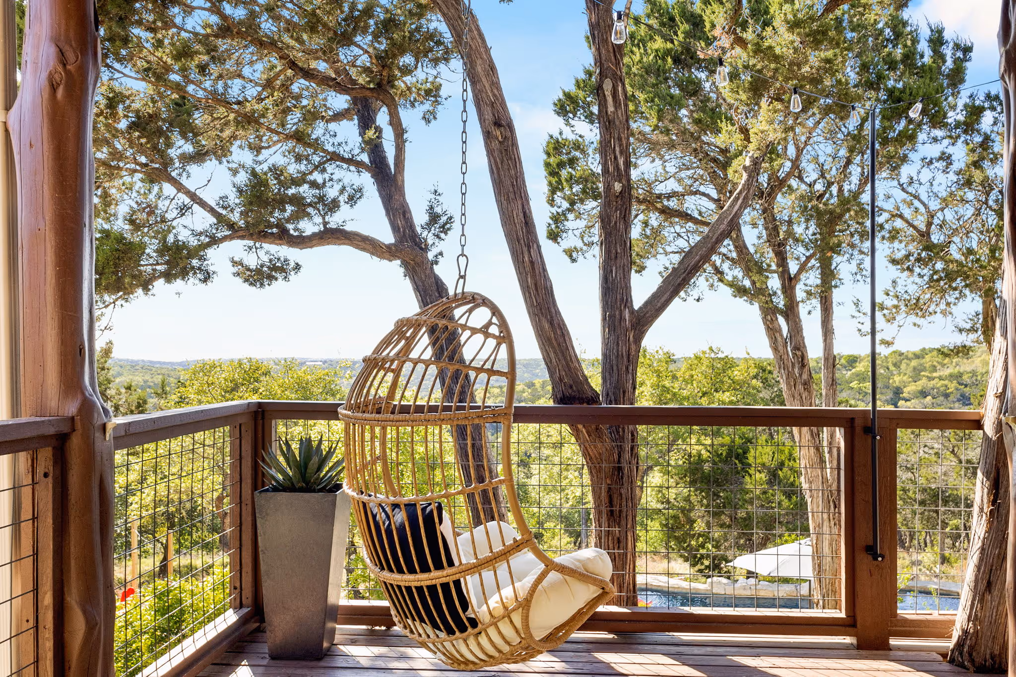 A balcony overlooking a wooded area with a swinging chair in view.