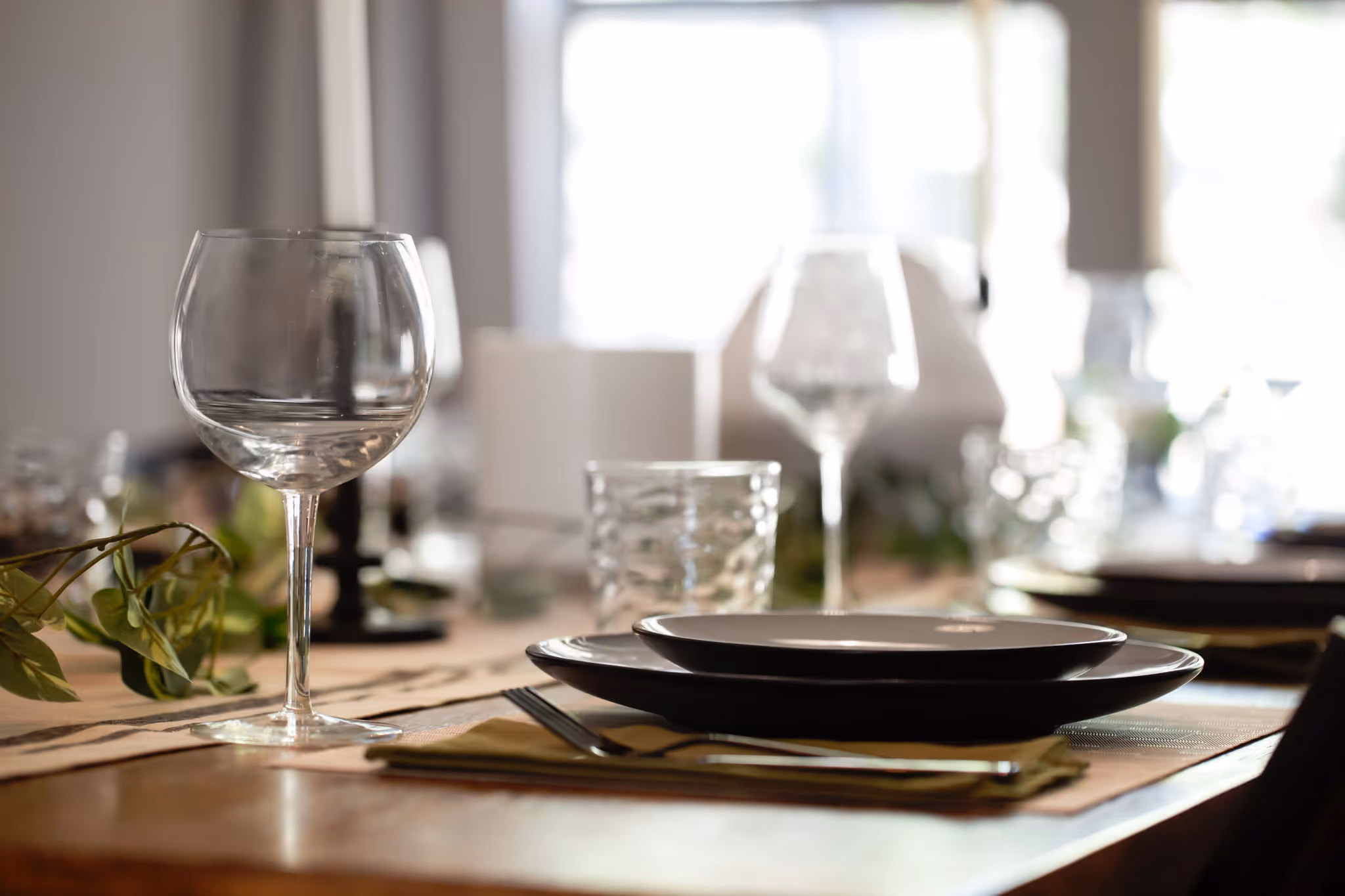 A bokeh shot of a wine glass on top of a dining table prepared for dinner.