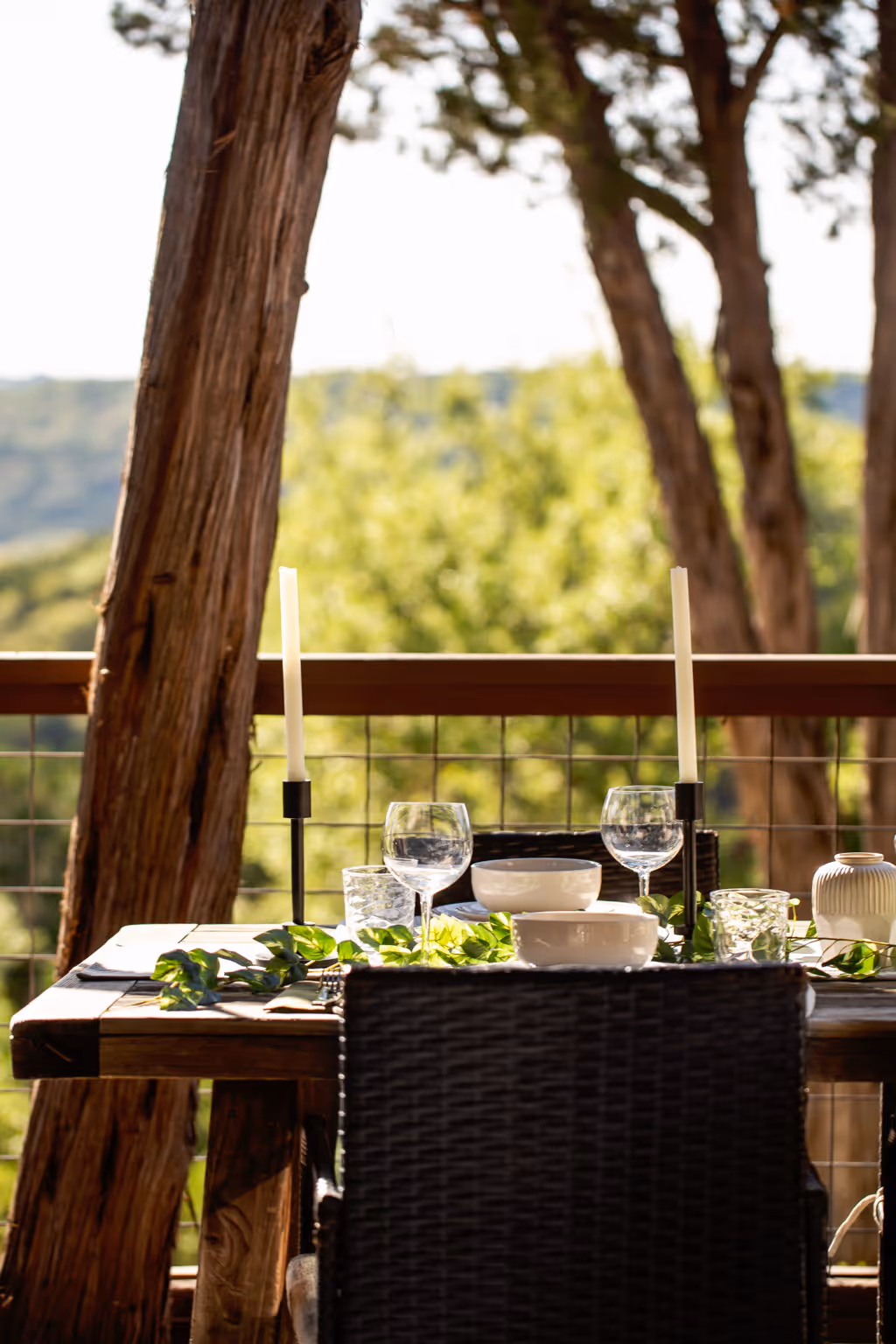 A dining table, set for dinner with candles, on an outdoor balcony overlooking the Texas hill country.