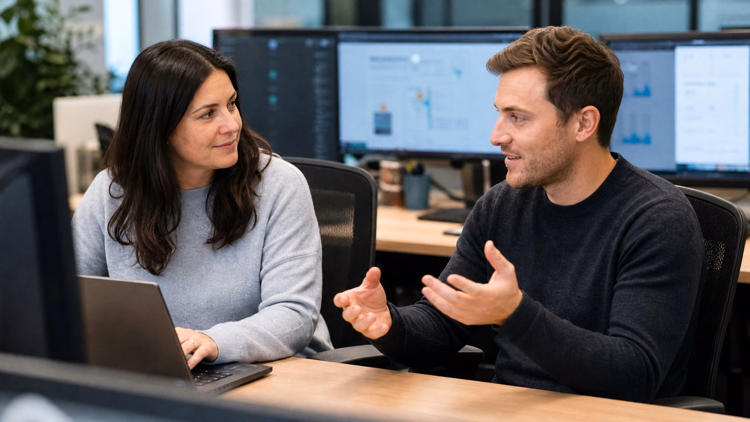 Woman taking notes on laptop, listening to man explain