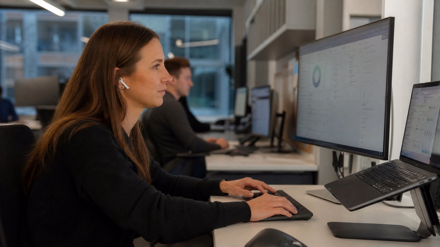 Woman with earbuds focused on computer screen at desk