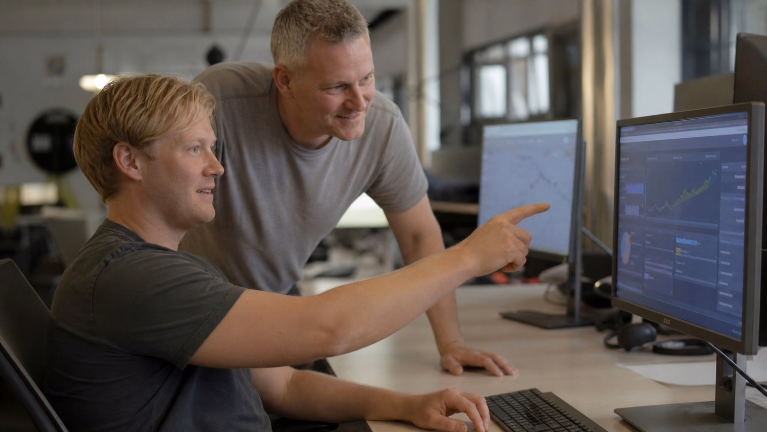 Mentor points to AI graph on monitor, colleague observes
