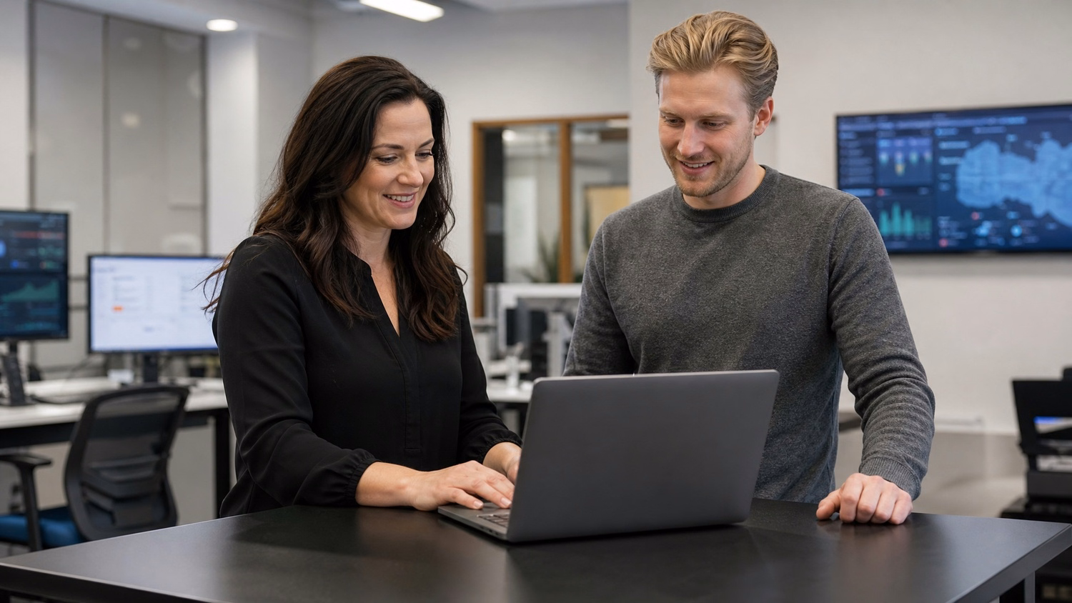 Two IT professionals review network inventory on laptop at standing table