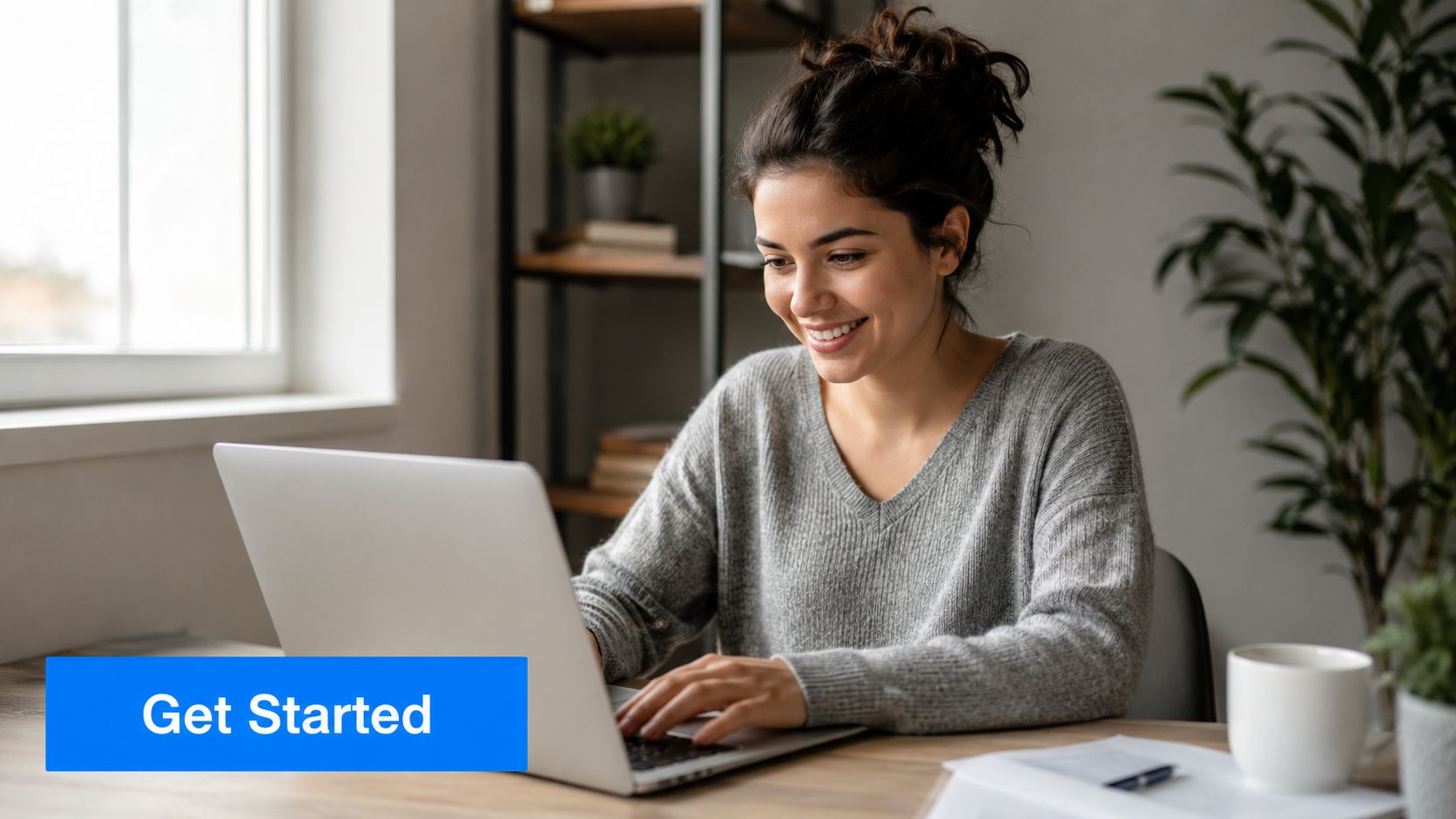 A happy young woman smiling while typing on her laptop at her desk in a home office.