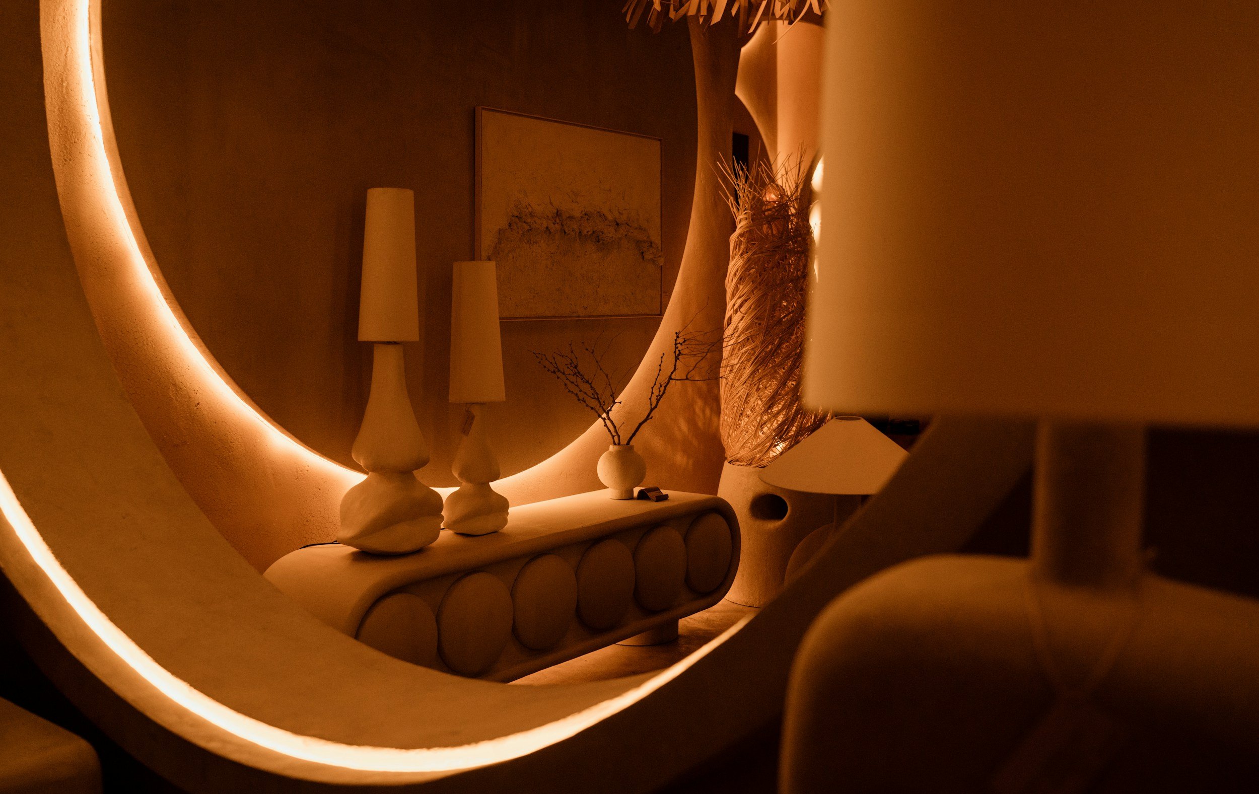 Warm ambient lighting in a modern interior with sculptural lamps, curved mirror, and minimalist decor.