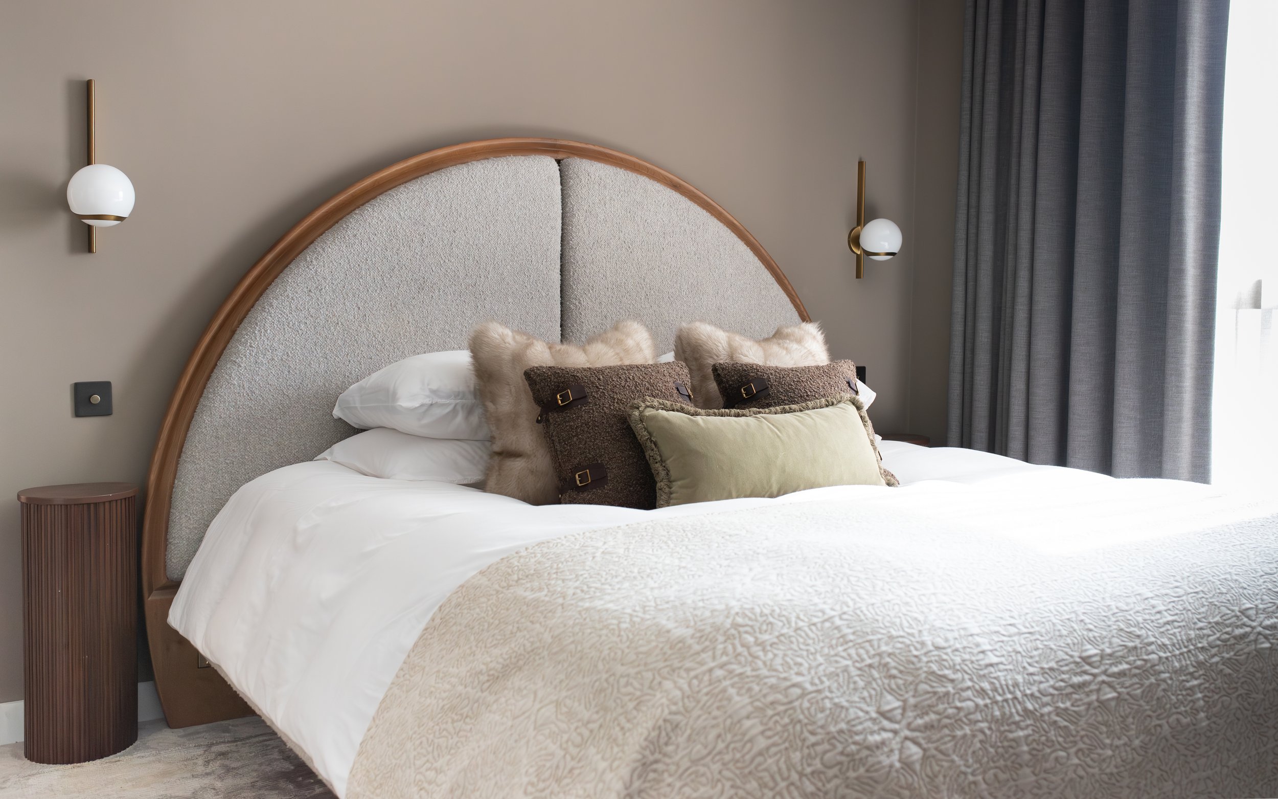 TXTURED luxury bedroom design in Manchester with curved boucle headboard, layered cushions, and warm neutral tones.