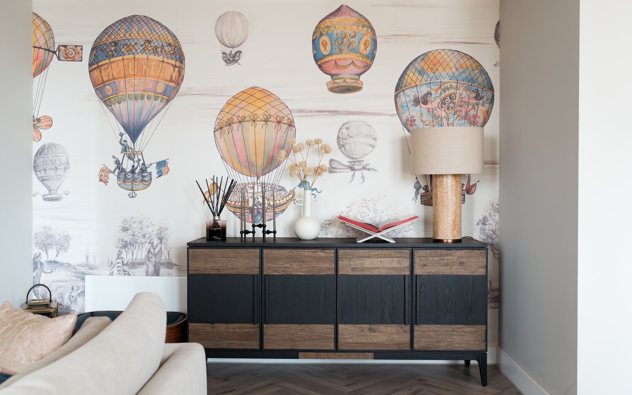 TXTURED luxury residential interior with statement hot air balloon wallpaper, black wood sideboard, and textured table lamp in Manchester apartment.