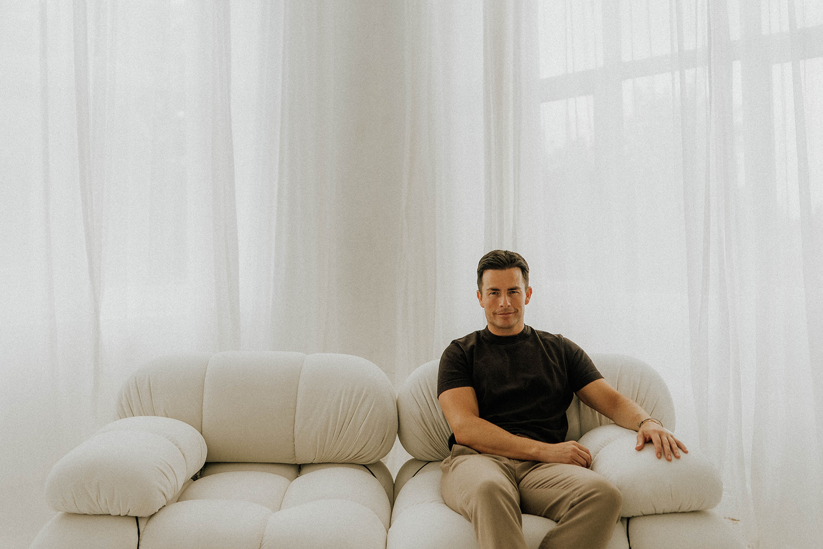 Simon Mayhew of TXTURED sitting on a cream textured sofa in a bright, minimalist interior
