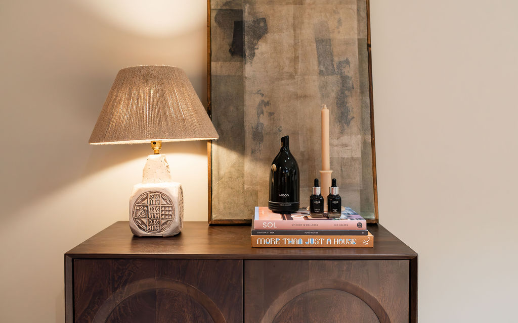 a lamp on a walnut unit with a candle and pile of books