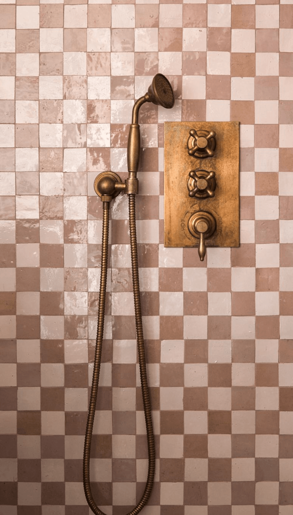 Pink and off white tiles in a shower with a gold shower head