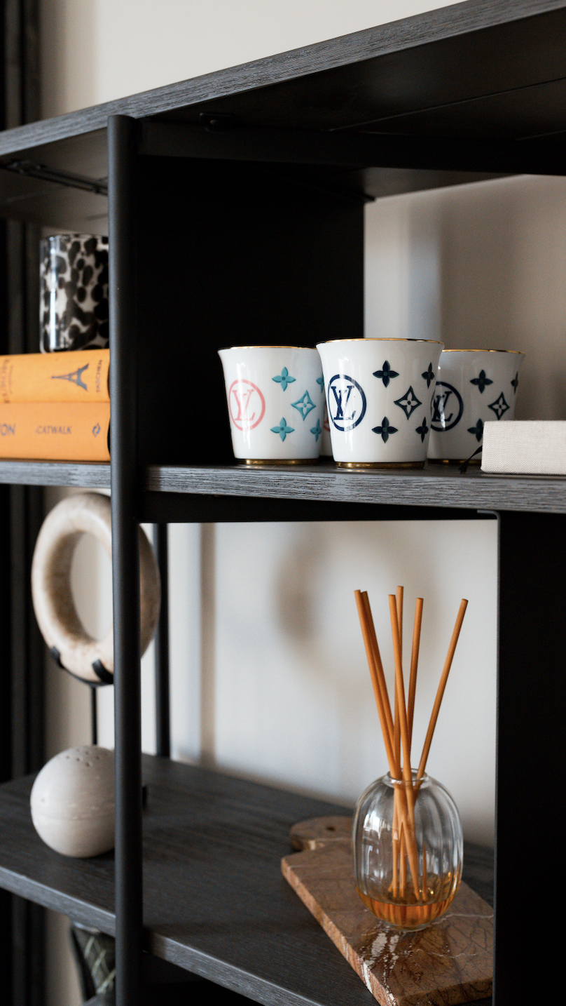 Open shelving in a TXTURED interior, styled with ceramic cups, books, sculptural objects and a glass reed diffuser, layered against dark timber shelves for a warm, tactile look.