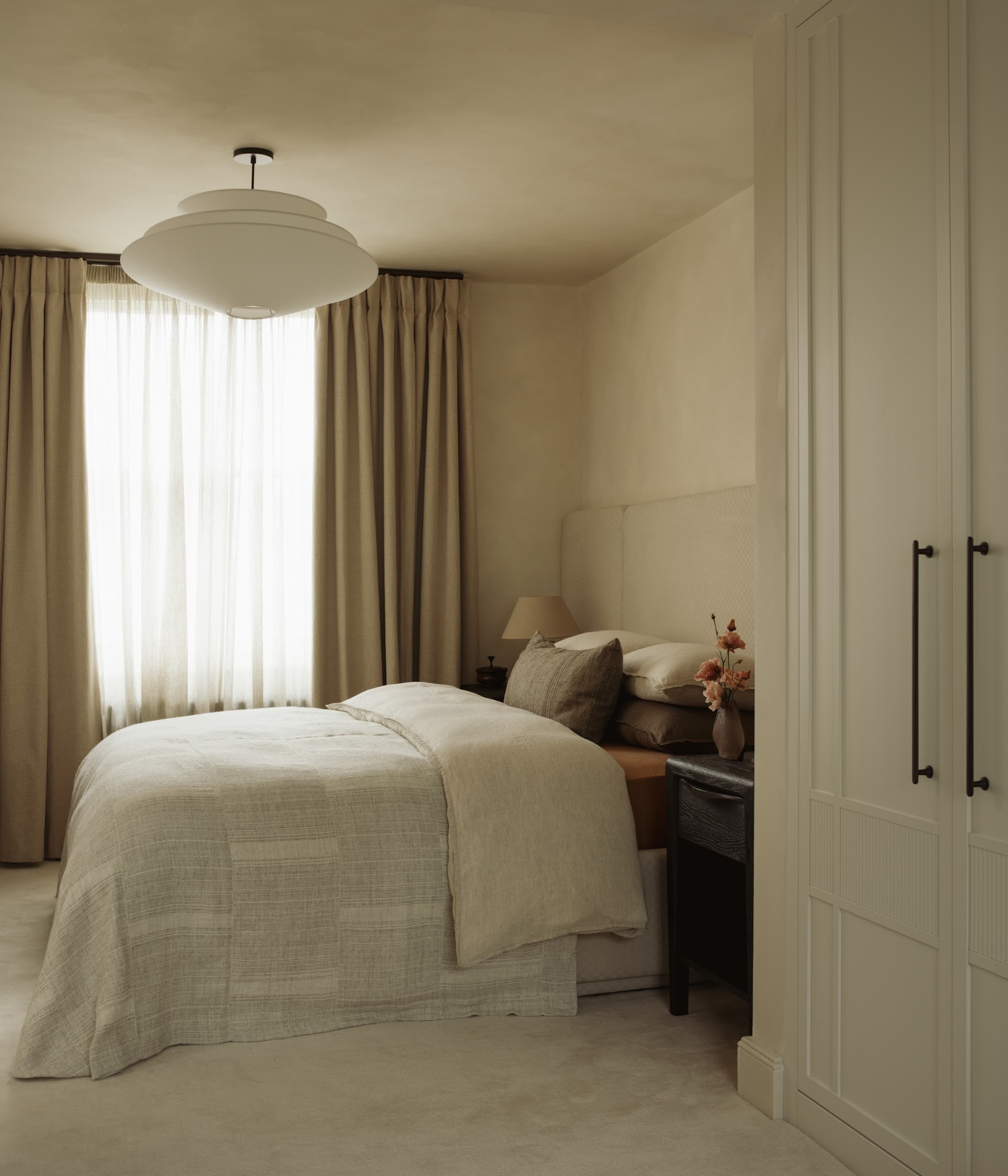 Bed with upholstered headboard, layered textiles and warm bedside lamplight in a London bedroom