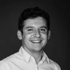 Portrait en noir et blanc d'un homme souriant portant une chemise claire sur un fond sombre.