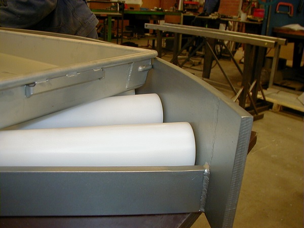 Freezer pans positioned on roller conveyor in seafood processing plant.