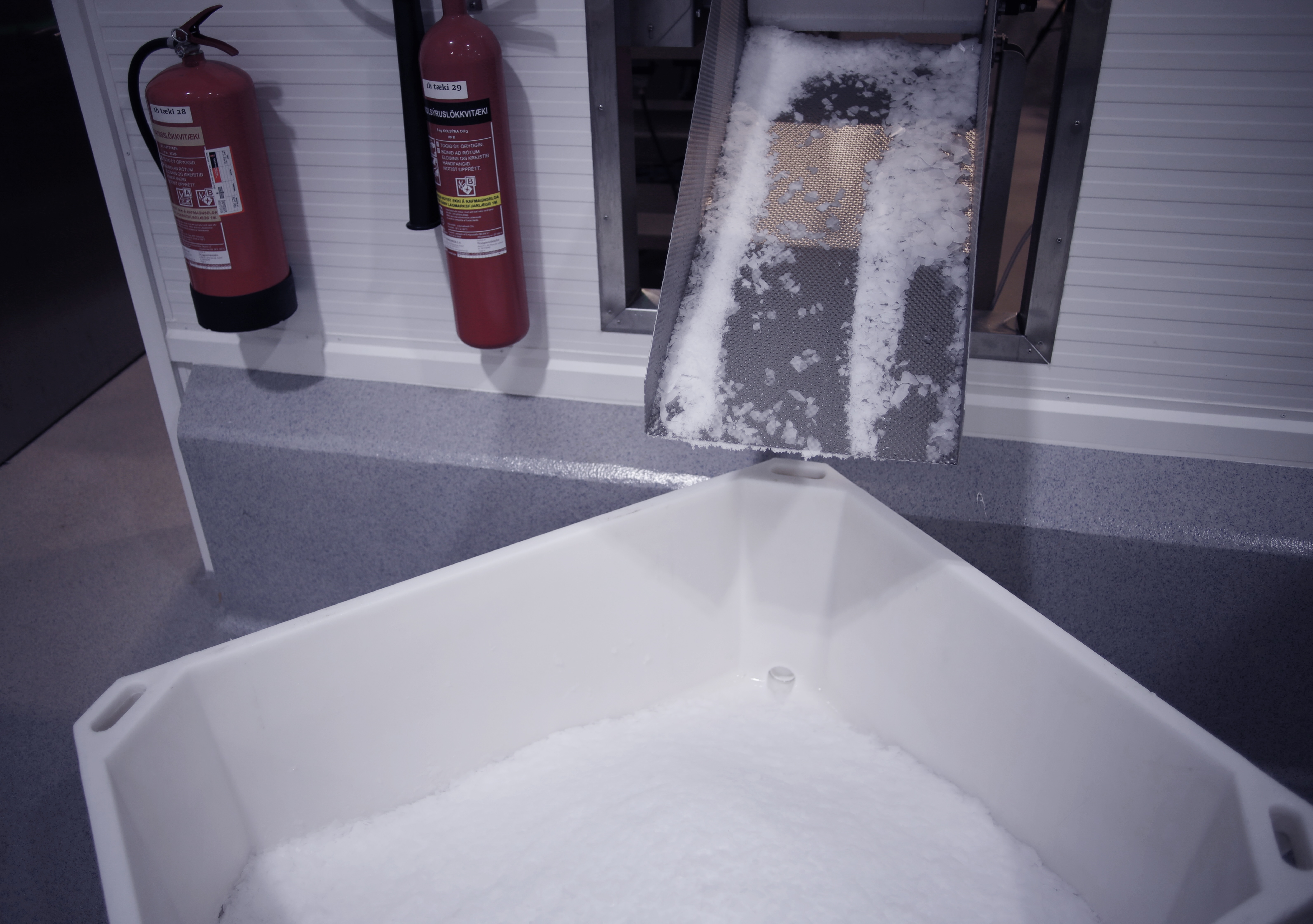 Flake ice falling from chute into white storage tub.