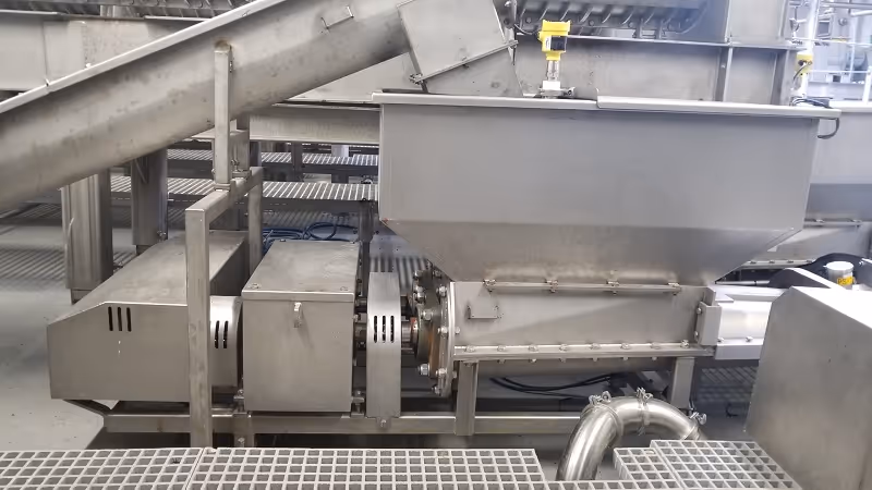 Side view of twin screw conveyor integrated into processing equipment.