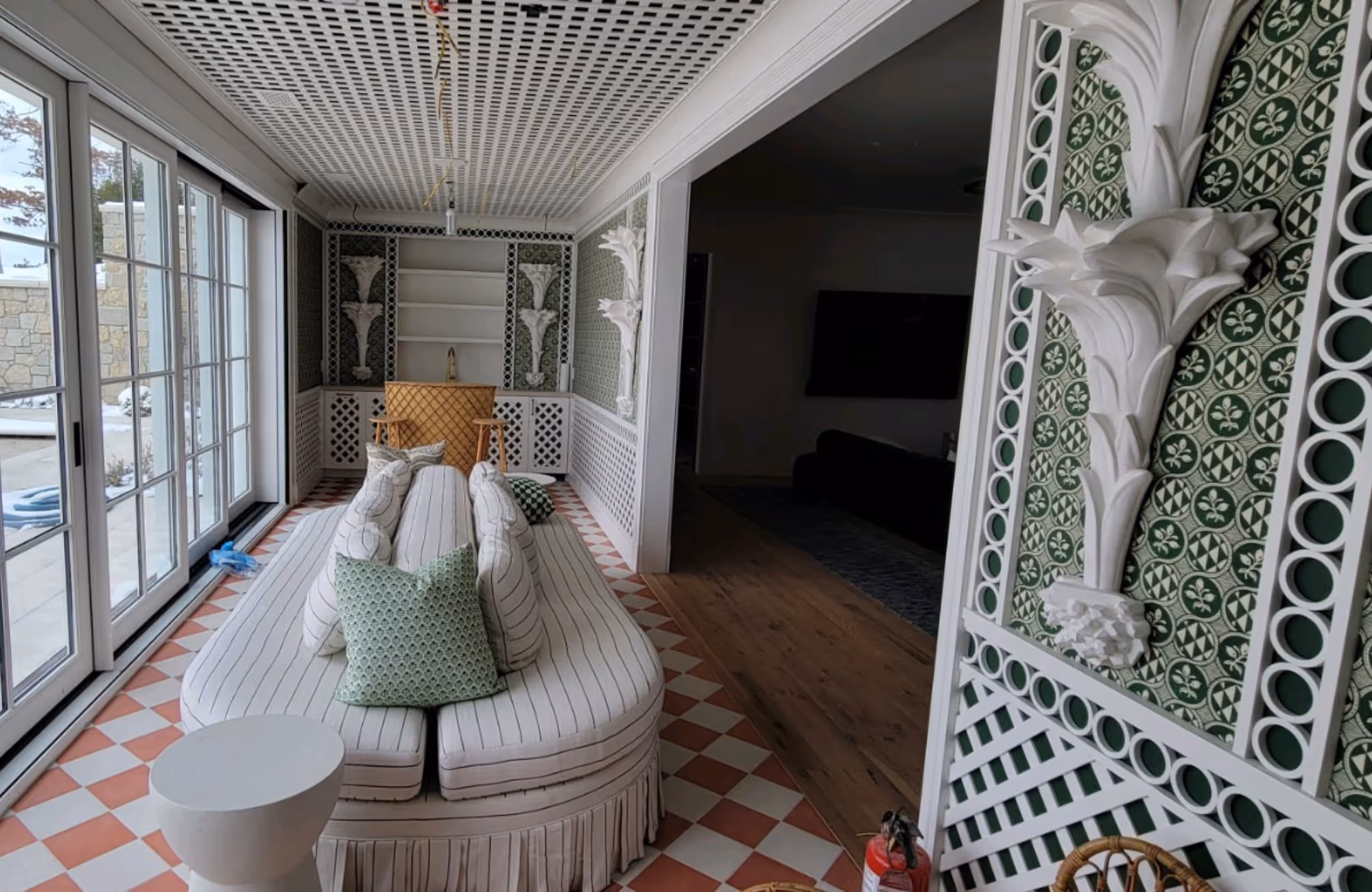 Indoor seating area with a striped white sofa adorned with patterned pillows, large sliding glass doors on the left, and intricate green and white decorative wall panels.