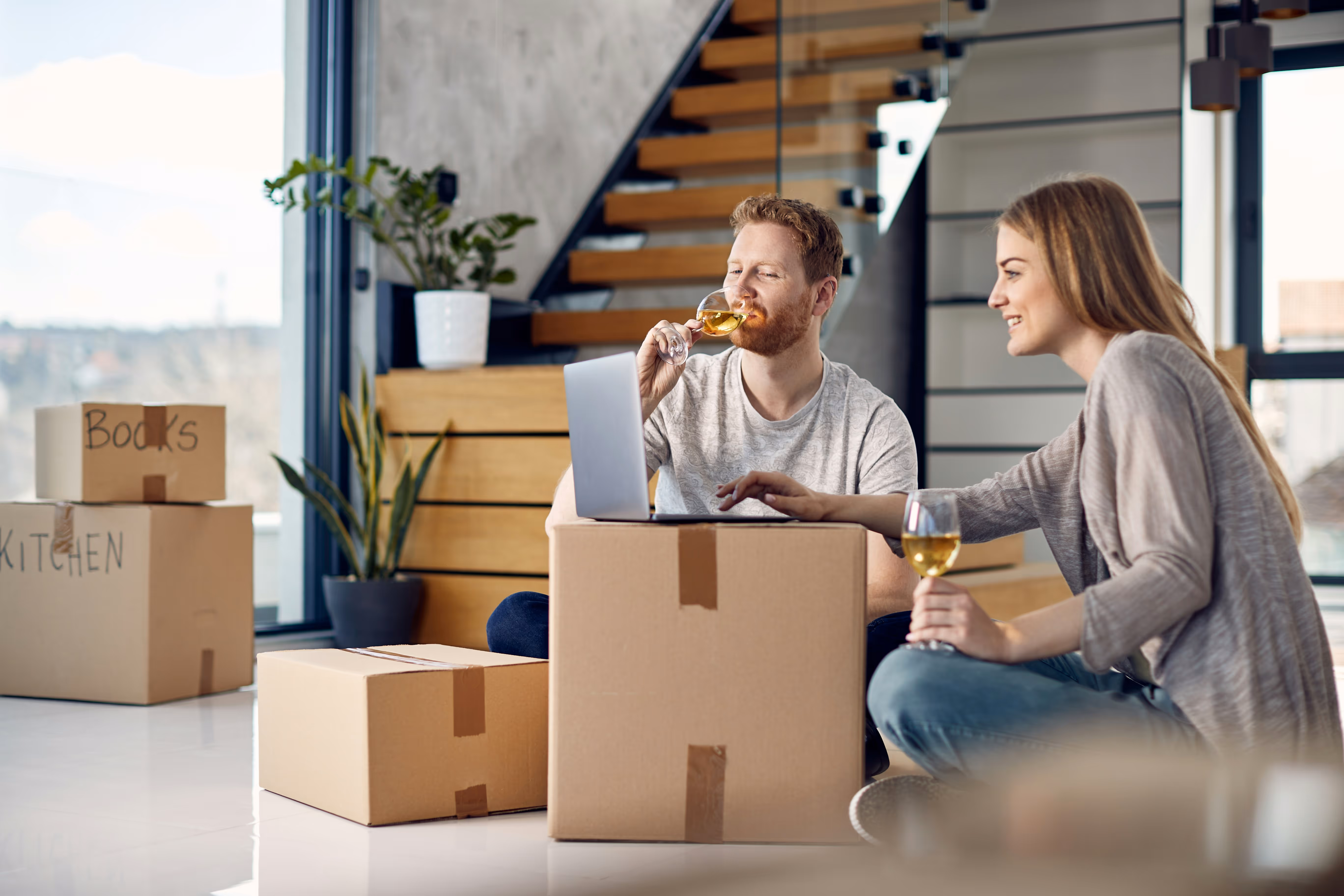 a couple sitting on the group with wine and moving boxes around them