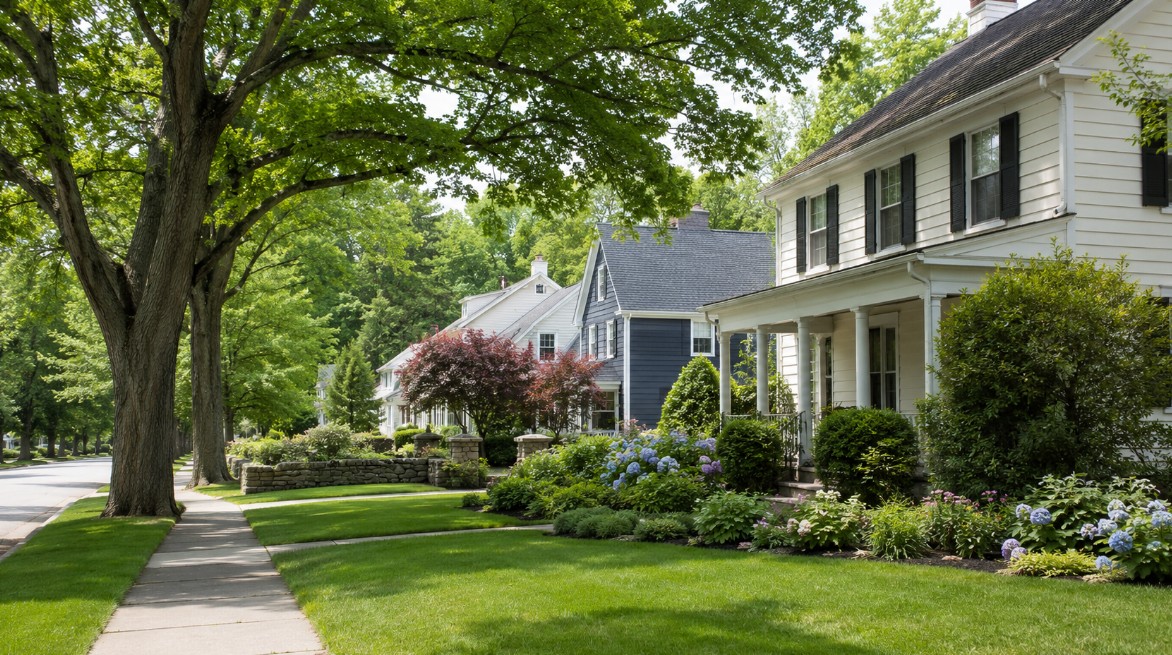 A realistic early-summer New England residential scene near Andover or North Andover, Massachusetts, with mature trees, clean sidewalks, well-kept homes, and a polished neighborhood feel.