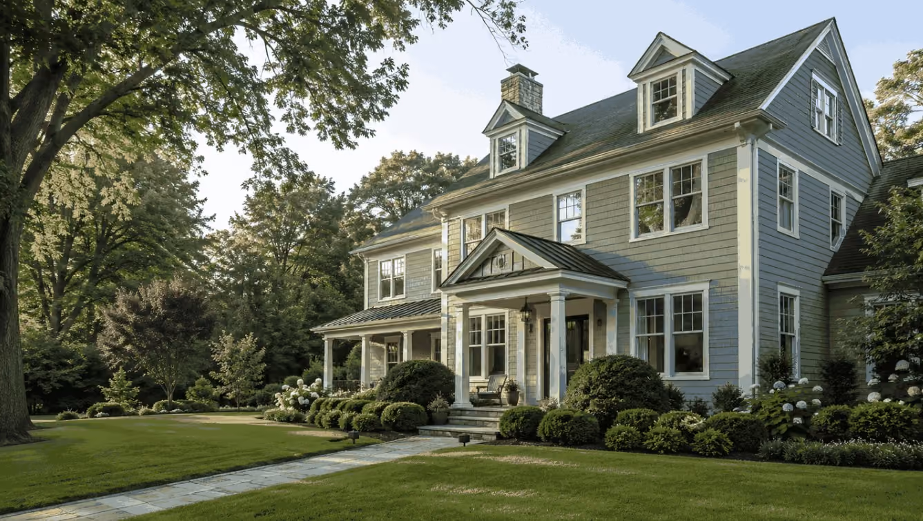 A polished higher-end New England home in the Andover or North Andover area, photographed during summer with mature landscaping, an inviting entry, clean architectural details, and a glimpse of an outdoor living area.