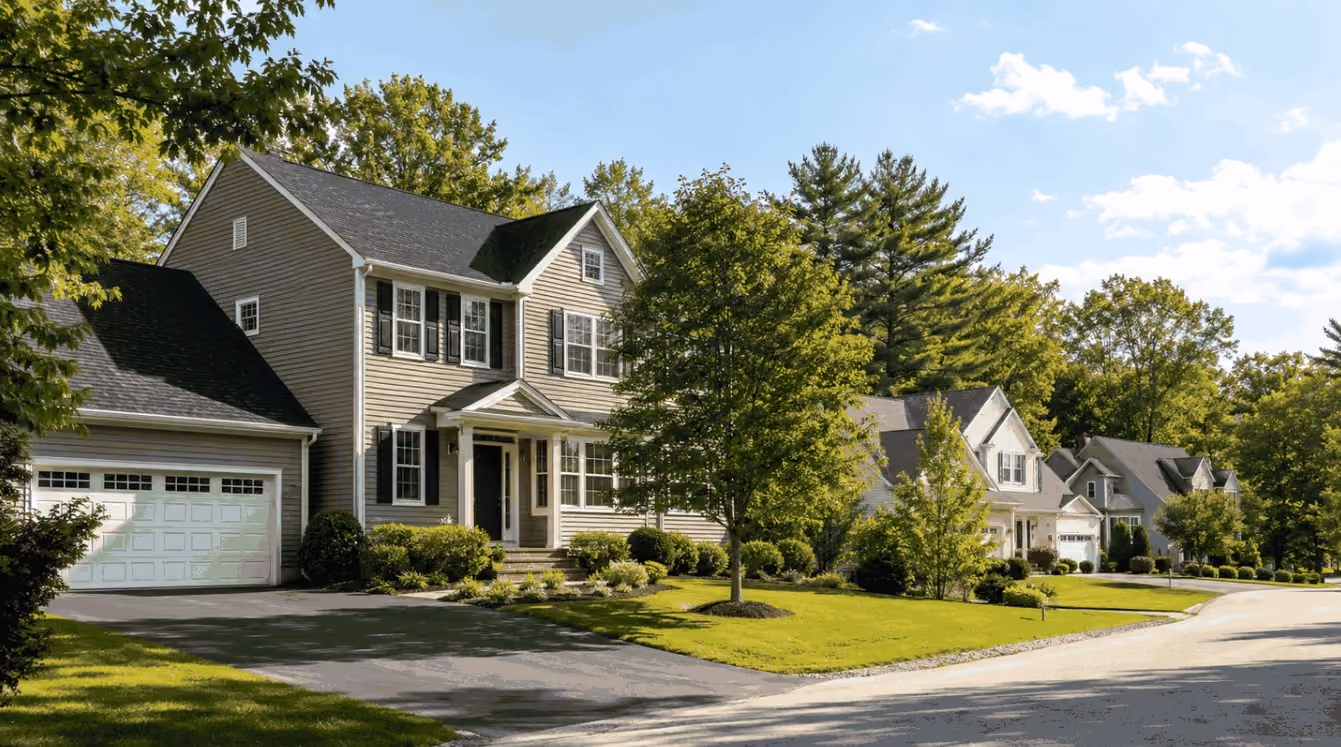 A carefully prepared New England-style home on a quiet Londonderry residential street during late summer, with trimmed landscaping, healthy greenery, fresh mulch, and warm natural light.