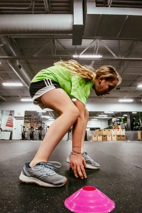 A young girl bends over to pick up a pink frisbee at Game Ready Fitness in Thornton, CO.