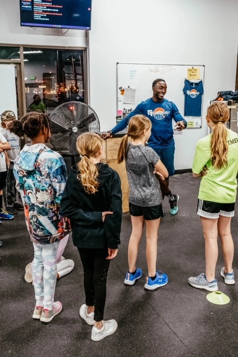 A man teaches a group of kids in a gym at Game Ready Fitness in Thornton, CO, promoting active learning and fitness.
