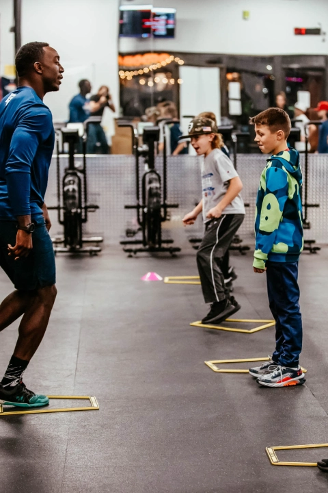 A group of children stands together in a gym at Game Ready Fitness in Thornton, CO, smiling and engaging with each other.