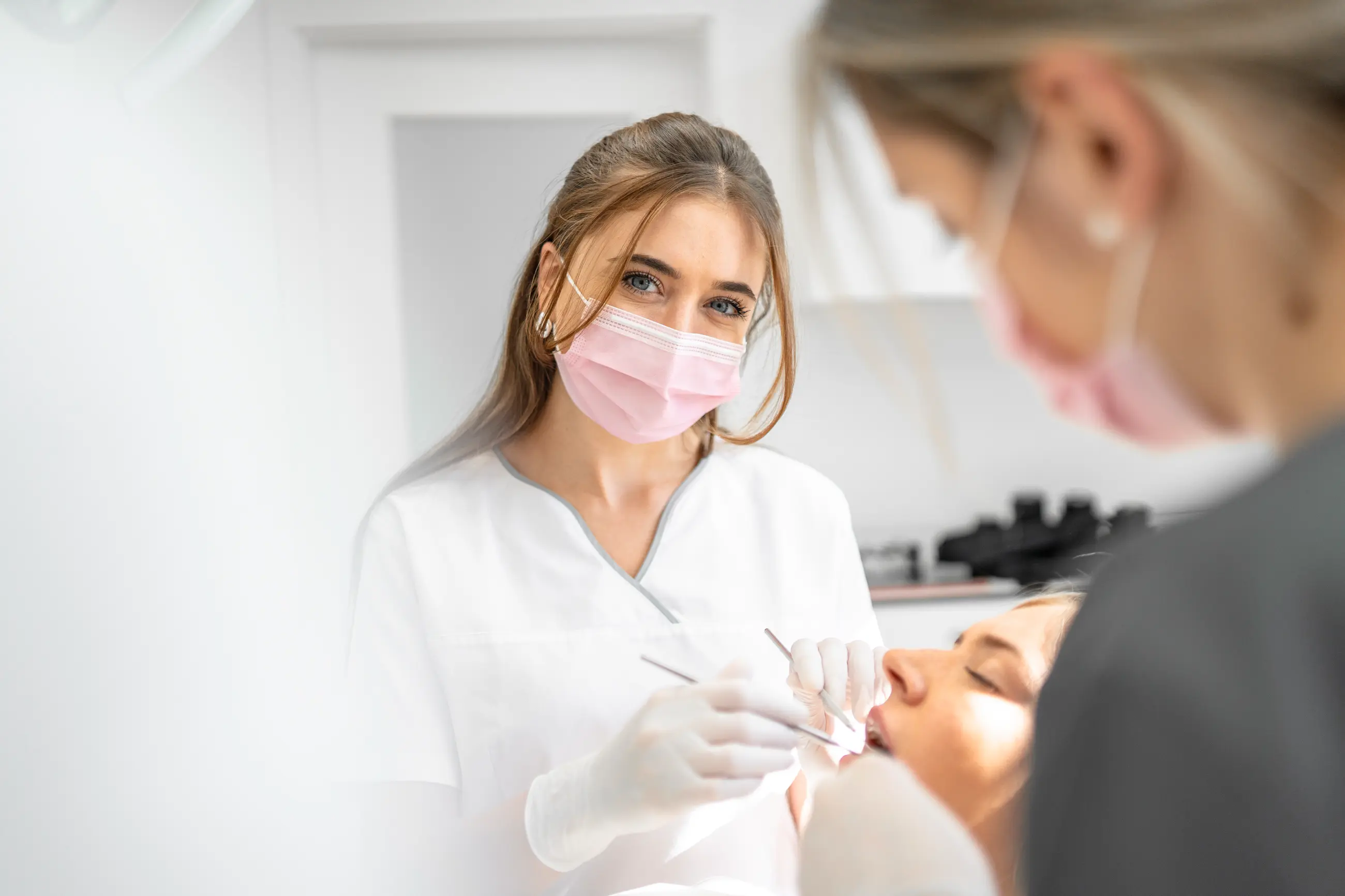 Zahnärztin mit Maske schaut in die Kamera während sie eine Patientin behandelt
