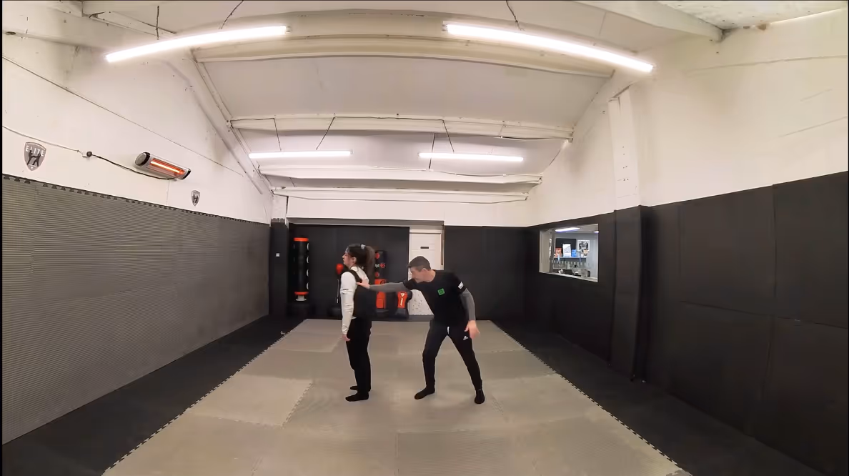 A woman is grabbed from behind in a dojo, demonstrating the correct technique to escape the situation.