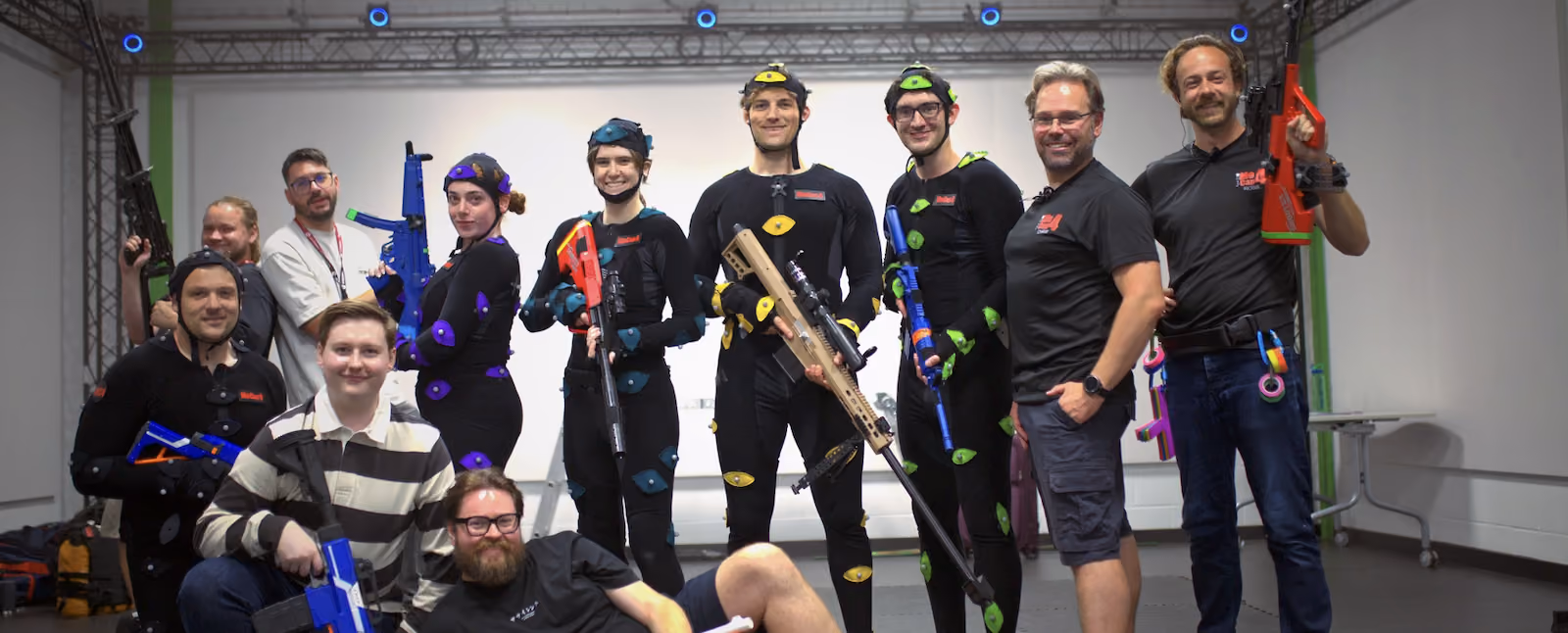 Performers wearing motion capture suit and markers, alongside production crew posing for a team photo inside XR Studios' OptiTrack motion capture studio in Essex