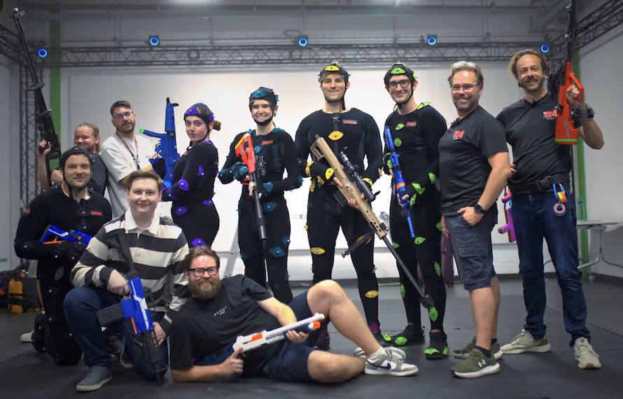 Performers wearing motion capture suit and markers, alongside production crew posing for a team photo inside XR Studios' OptiTrack motion capture studio in Essex