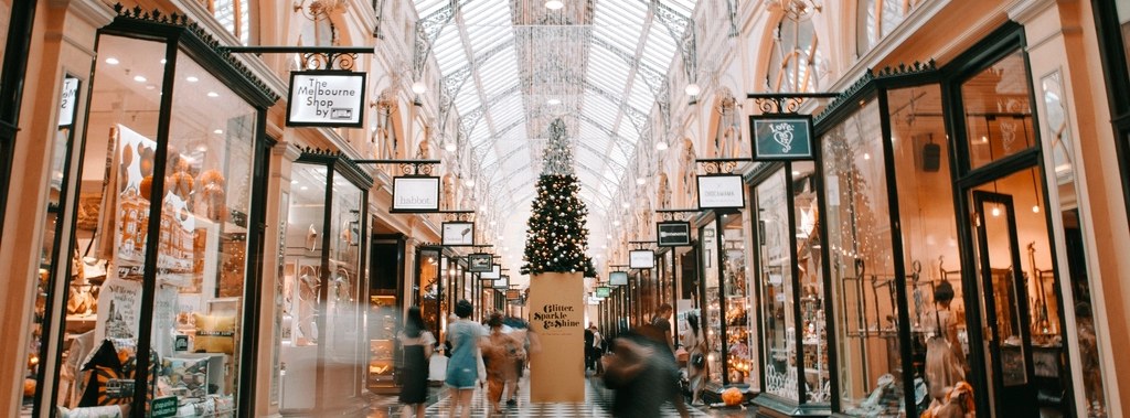 Holiday shoppers walking through a decorated shopping arcade with a Christmas tree
