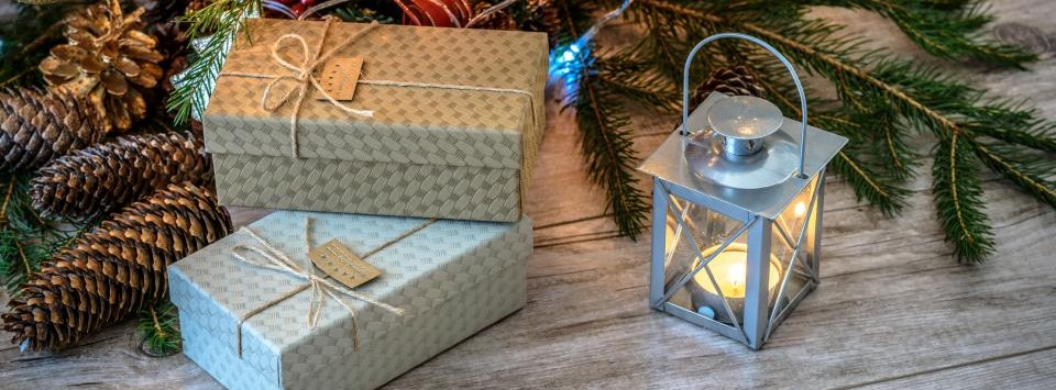 Wrapped holiday gifts with pine cones, greenery, and a lit lantern on a wooden table