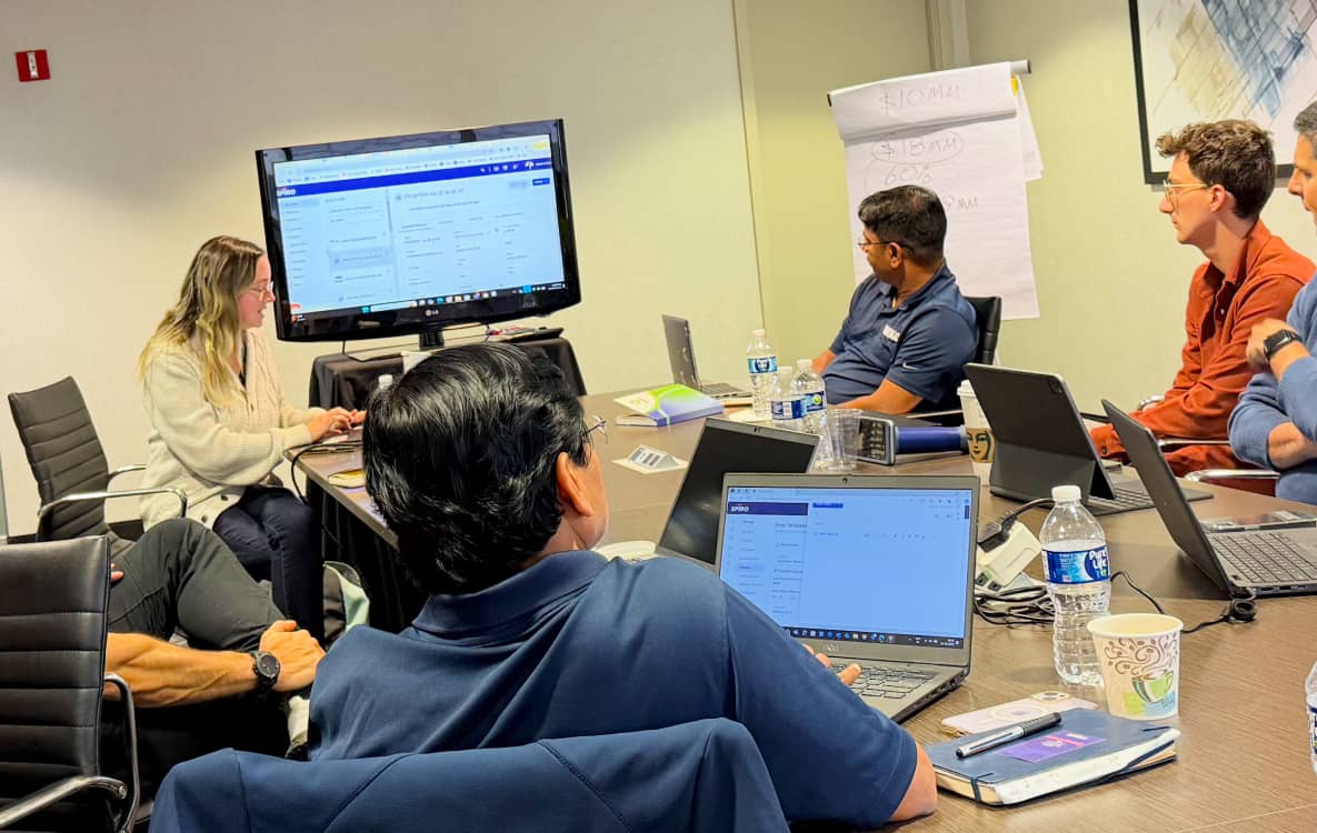Spiro team onboarding a manufacturing client, gathered around laptops and a large screen during an in-person training session.