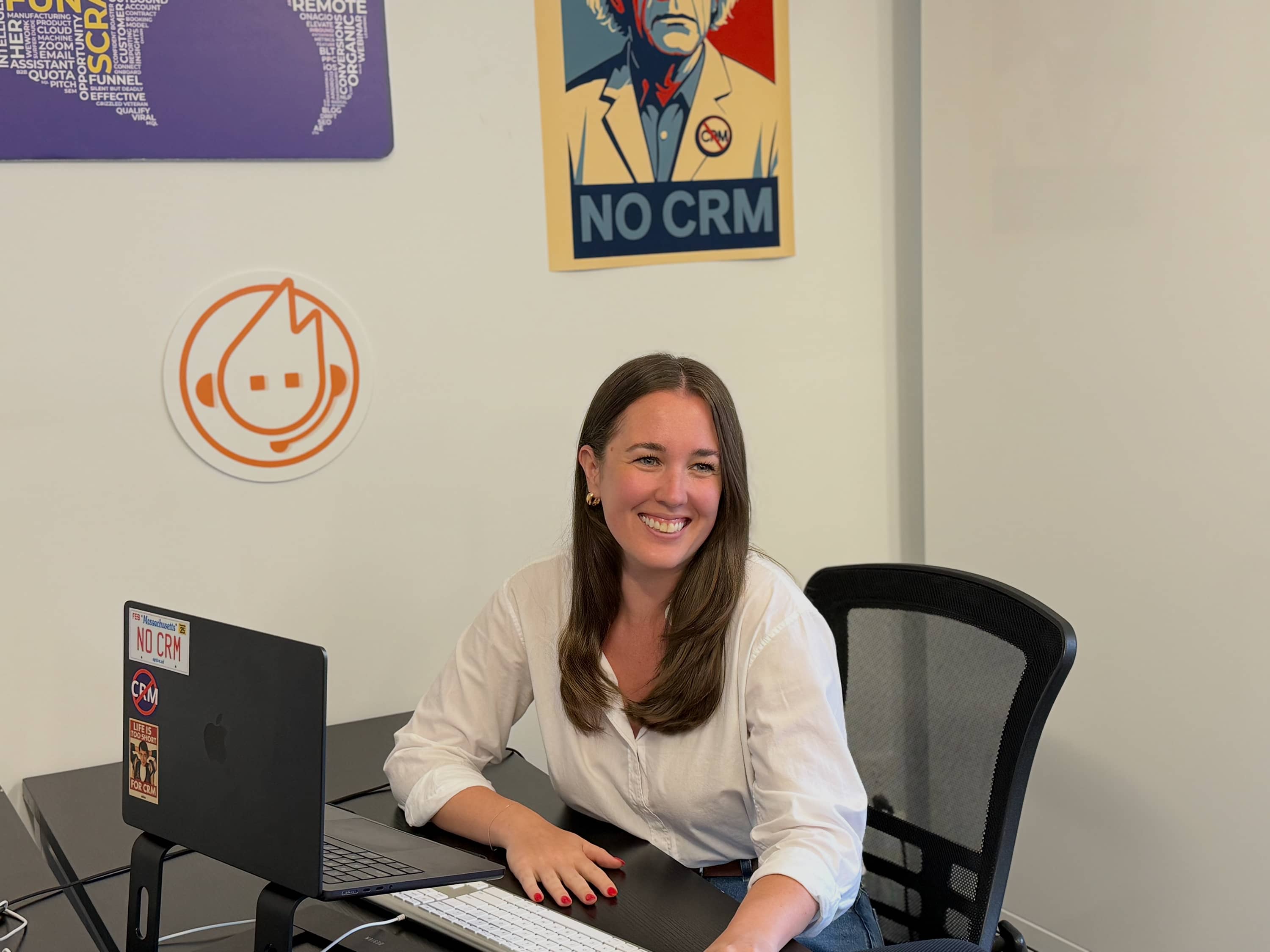 Spiro team member at a laptop with “No CRM” posters in the background, representing Spiro’s hands-on onboarding and full-service support for manufacturers.