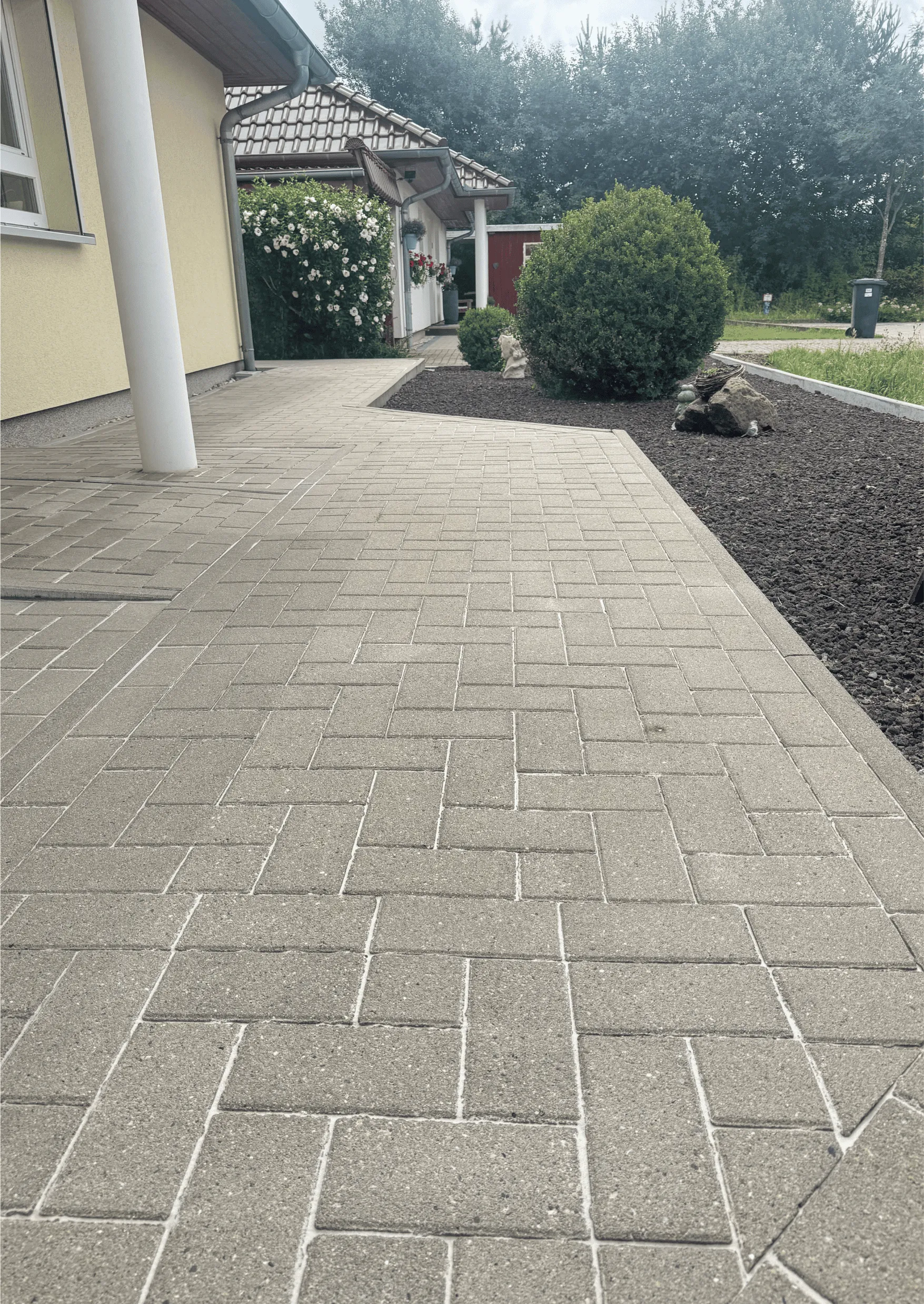 Eingangsbereich mit frisch gereinigten hellgrauen Pflastersteinen und gepflegtem Garten